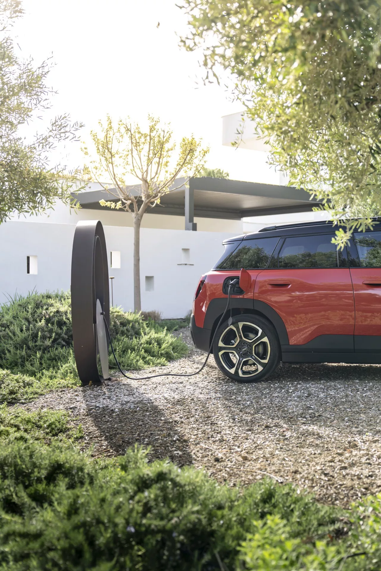 SUV Mini Aceman (J05) 2024 en rouge vif, mettant en avant le quart arrière de la voiture et le design de la roue avec une station de charge pour véhicule électrique en vue, suggérant une technologie de transport durable.
