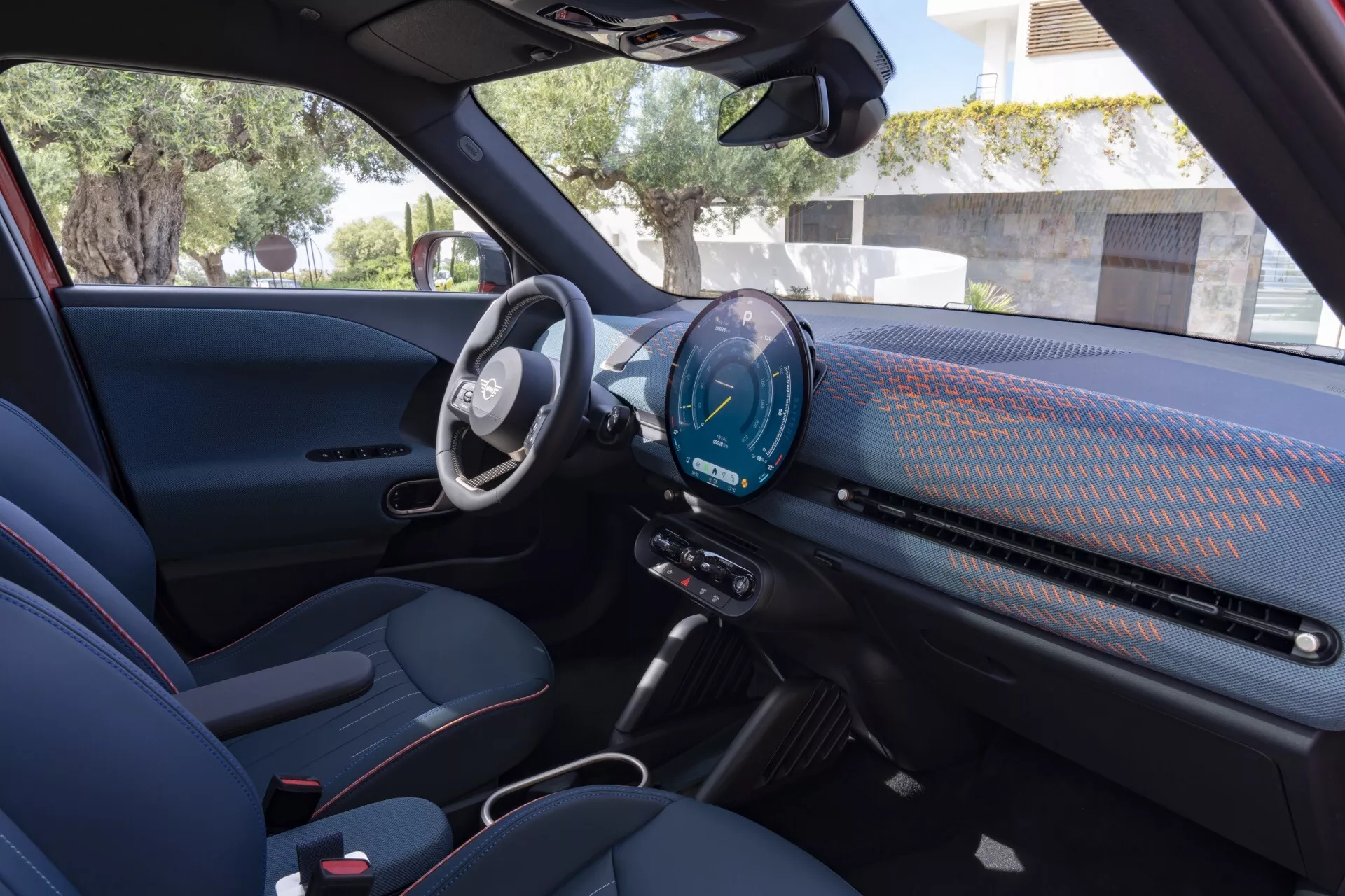 Vue intérieure du Mini Aceman 2024 (JO5) depuis le côté passager, mettant en évidence son cockpit numérique, écran tactile central d'infodivertissement avec fonctionnalités de connectivité, panneau de contrôle minimaliste, sièges sportifs bicolores avec coutures accentuées en rouge et caractéristiques technologiques et de sécurité avancées.