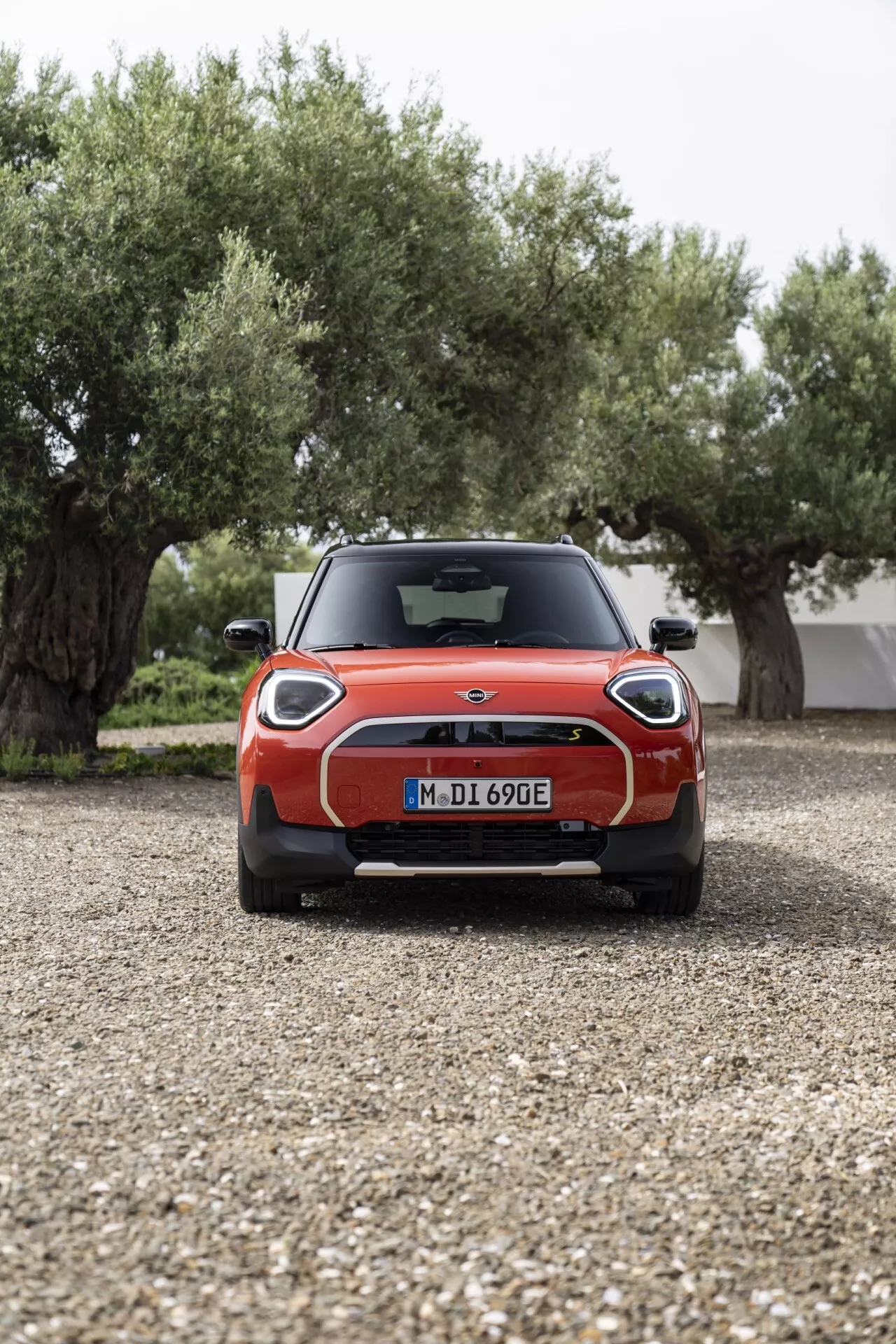 Mini Aceman 2024 (J05) en rouge, présentant des feux arrière LED distinctifs en forme de Union Jack, un becquet arrière, des capteurs de stationnement et une indication de modèle électrique depuis une vue arrière directe sur gravier avec des oliviers et un bâtiment en arrière-plan