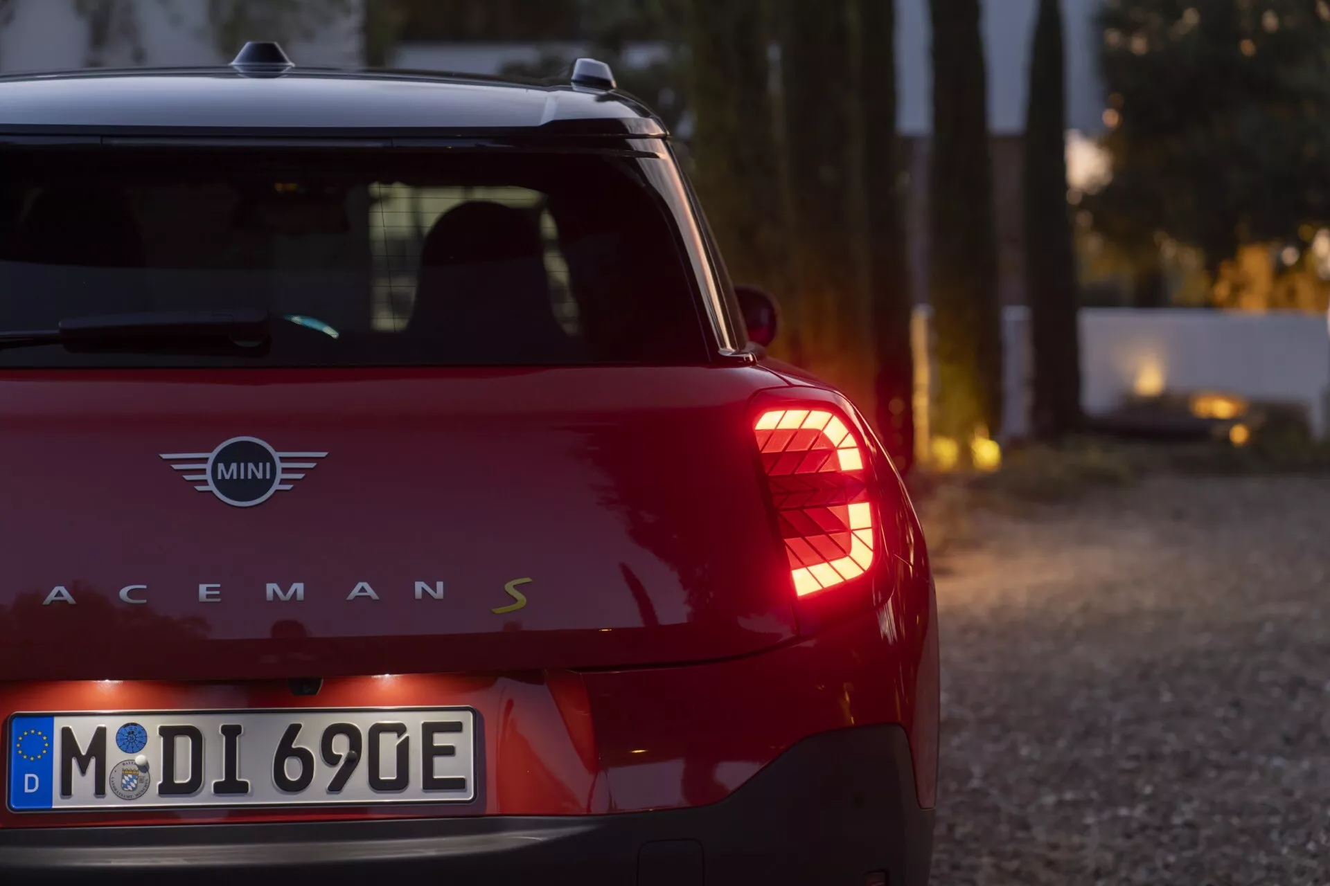 Vue rapprochée de l'arrière d'un modèle rouge MINI Paceman S 2024 (J05) sous un éclairage doux, mettant en avant les feux arrière verticaux distinctifs et les détails métalliques du logo.