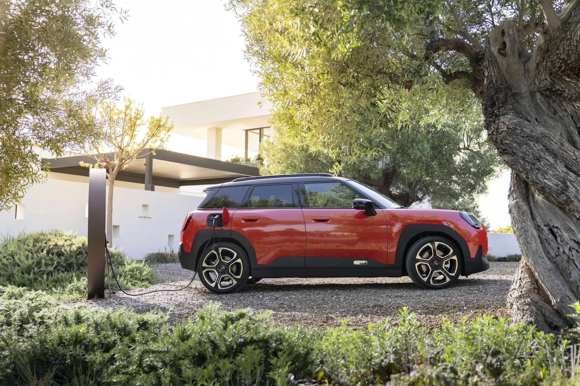 Mini Aceman 2024 (J05) présentée dans un cadre luxueux, offrant un design moderne de SUV bicolore, toit noir contrastant, vitres teintées et jantes alliage sportives, garée sur une allée de gravier avec verdure résidentielle et une possible station de recharge VE indiquant une technologie avancée et un souci écologique
