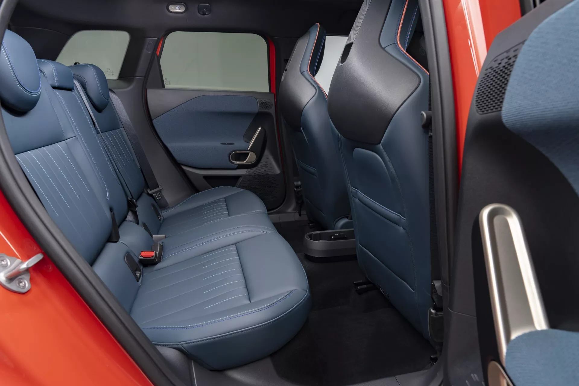 Vue intérieure du Mini Aceman (J05) 2024 se concentrant sur le compartiment passager arrière, montrant l'habillage des sièges en tissu à motifs et la conception des sièges pour un confort accru, avec une porte visible dotée de commandes de vitres électriques et de grilles pour le système audio.