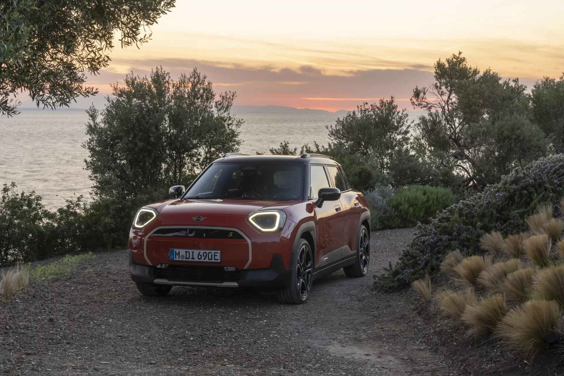 Mini Aceman (J05) 2024 en bicolore garée sur un chemin de gravier près de la mer au lever/coucher du soleil présentant calandre avant, phares LED, roues en alliage et fonctionnalités électriques sur fond côtier
