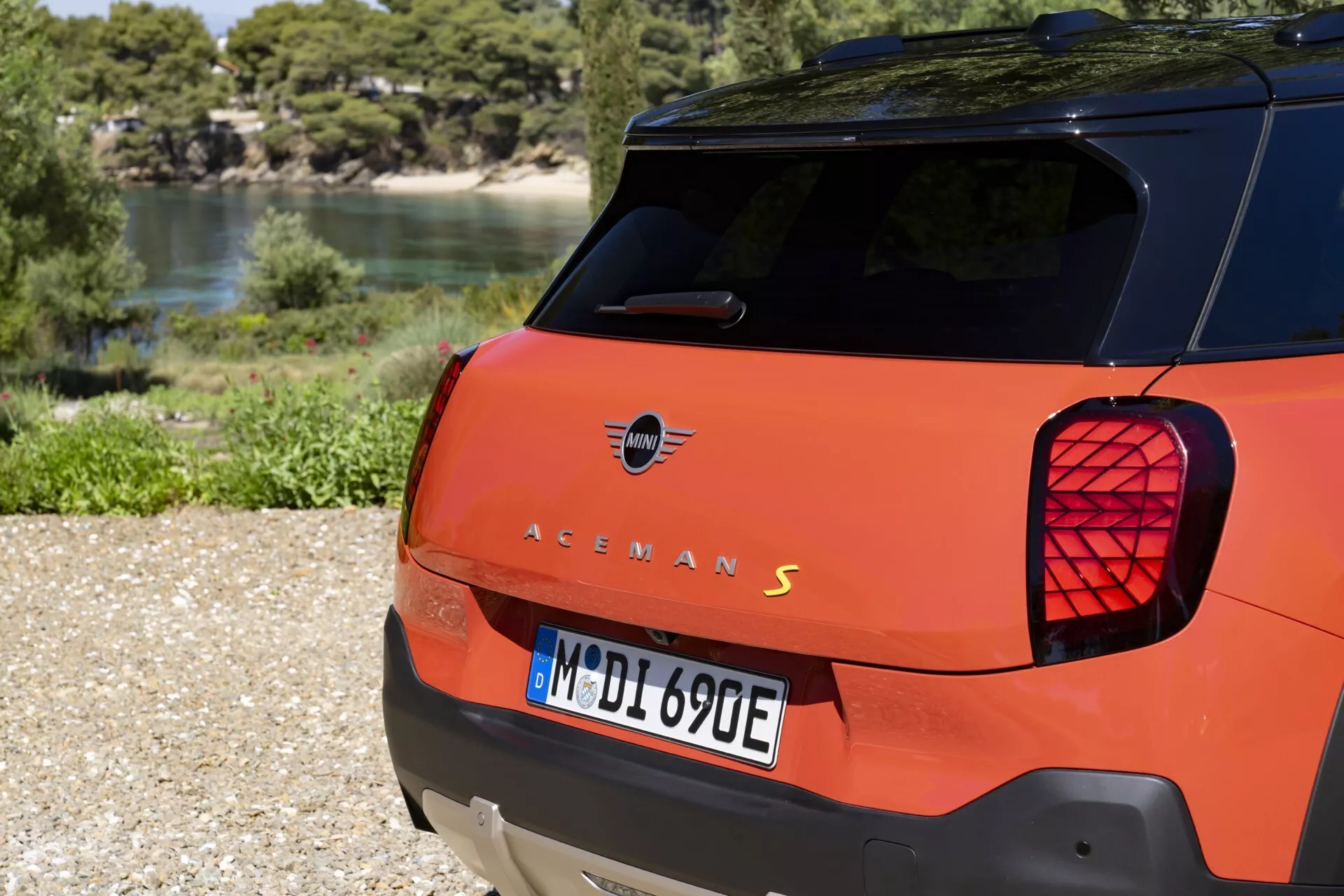 Vue arrière d'une hatchback orange présentant des feux arrière distinctifs avec un motif Union Jack, modèle 'S' électrique possible, garée en extérieur sur gravier avec un arrière-plan naturel
