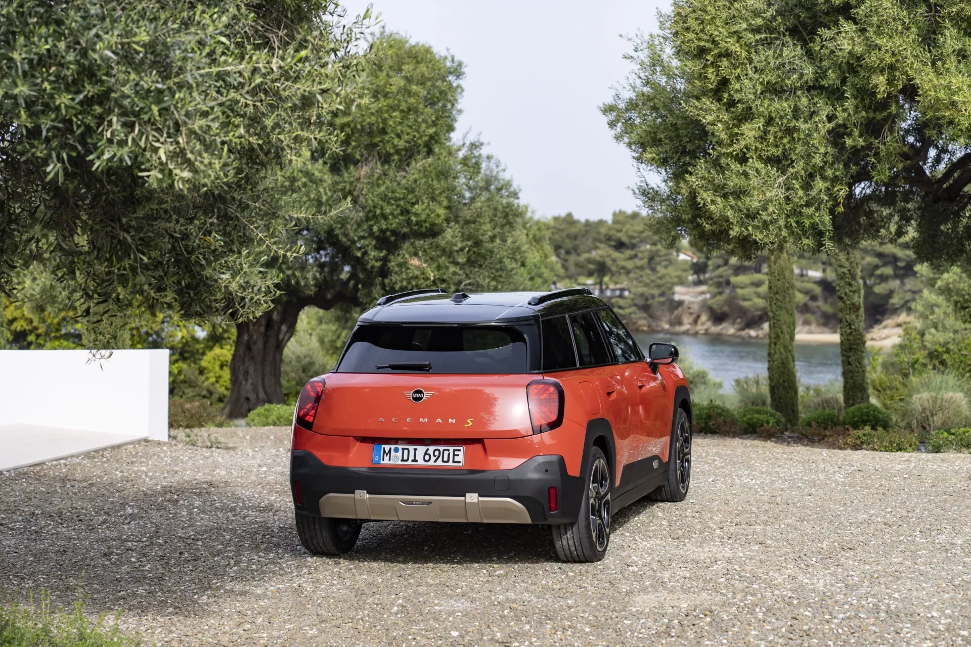 Vue arrière du Mini Aceman (J05) 2024 mettant en avant son schéma de couleurs bicolore, ses élégants feux arrière LED et son spoiler arrière sportif sur un fond naturel avec du gravier, des arbres et de l'eau, suggérant une capacité électrique ou hybride