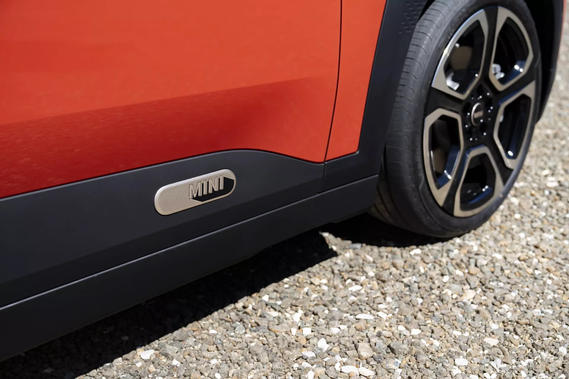 Gros plan sur le Mini Aceman 2024 (J05) montrant le côté inférieur de la voiture, la roue arrière à design multibranches, la couleur vibrante rouge de la carrosserie et le bas de caisse distinctif avec emblème MINI