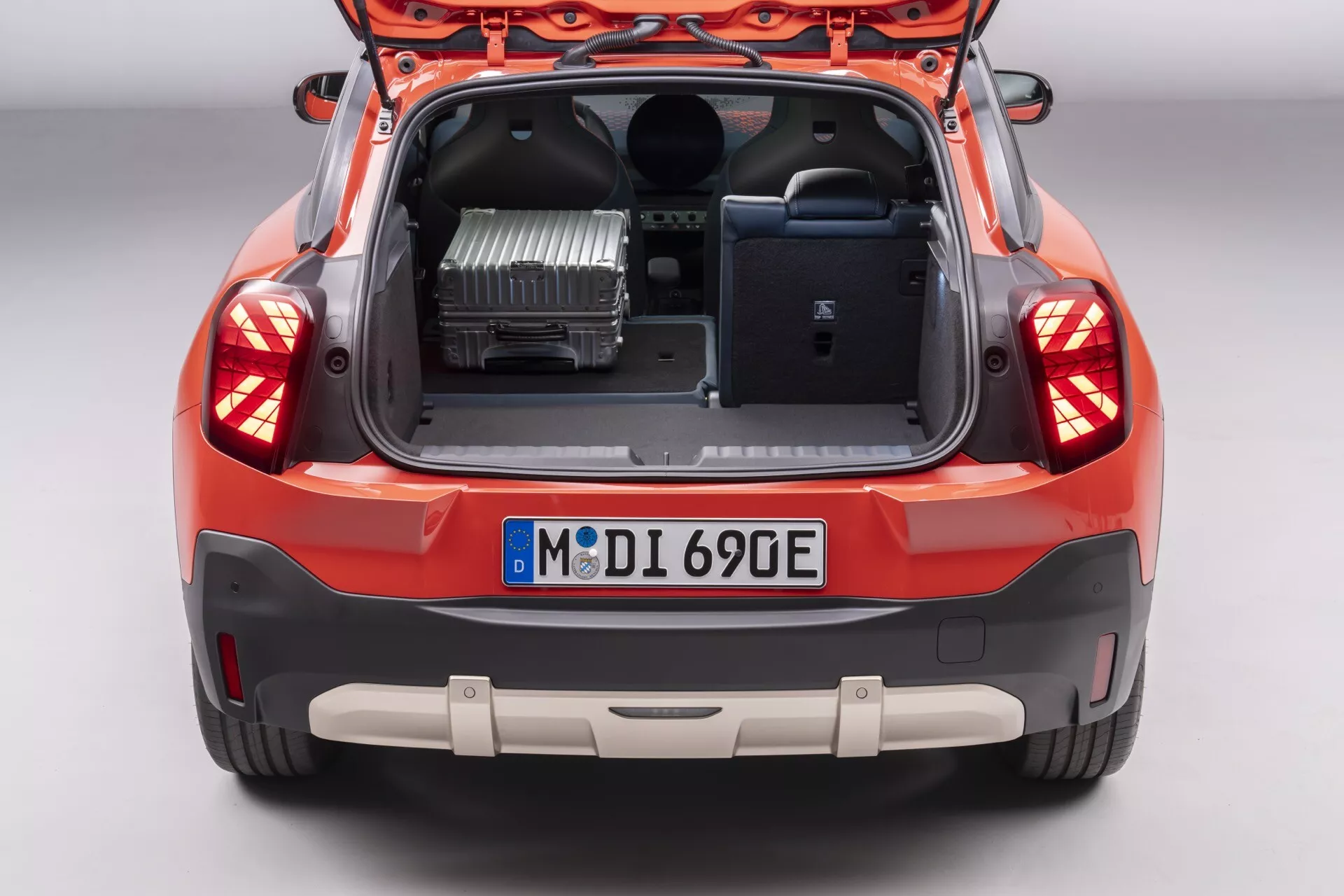 Image arrière du Mini Aceman 2024 (J05) avec hayon ouvert montrant l'espace du coffre et un aperçu de l'intérieur, caractérisée par des feux arrière LED, plaque d'immatriculation, pare-chocs arrière avec capteurs de stationnement, design à deux tons du pare-chocs, composant de motorisation électrique visible et panneau intérieur du hayon avec poignée