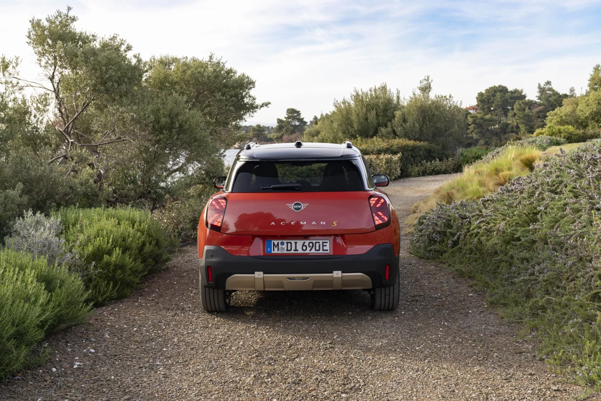 Vue arrière du Mini Aceman 2024 (JO5) mettant en lumière les feux arrière LED, le badge électrique/hybride, les capteurs d'assistance au parking, le système de caméra arrière et le porte-bagages sur un chemin de terre avec un décor naturel