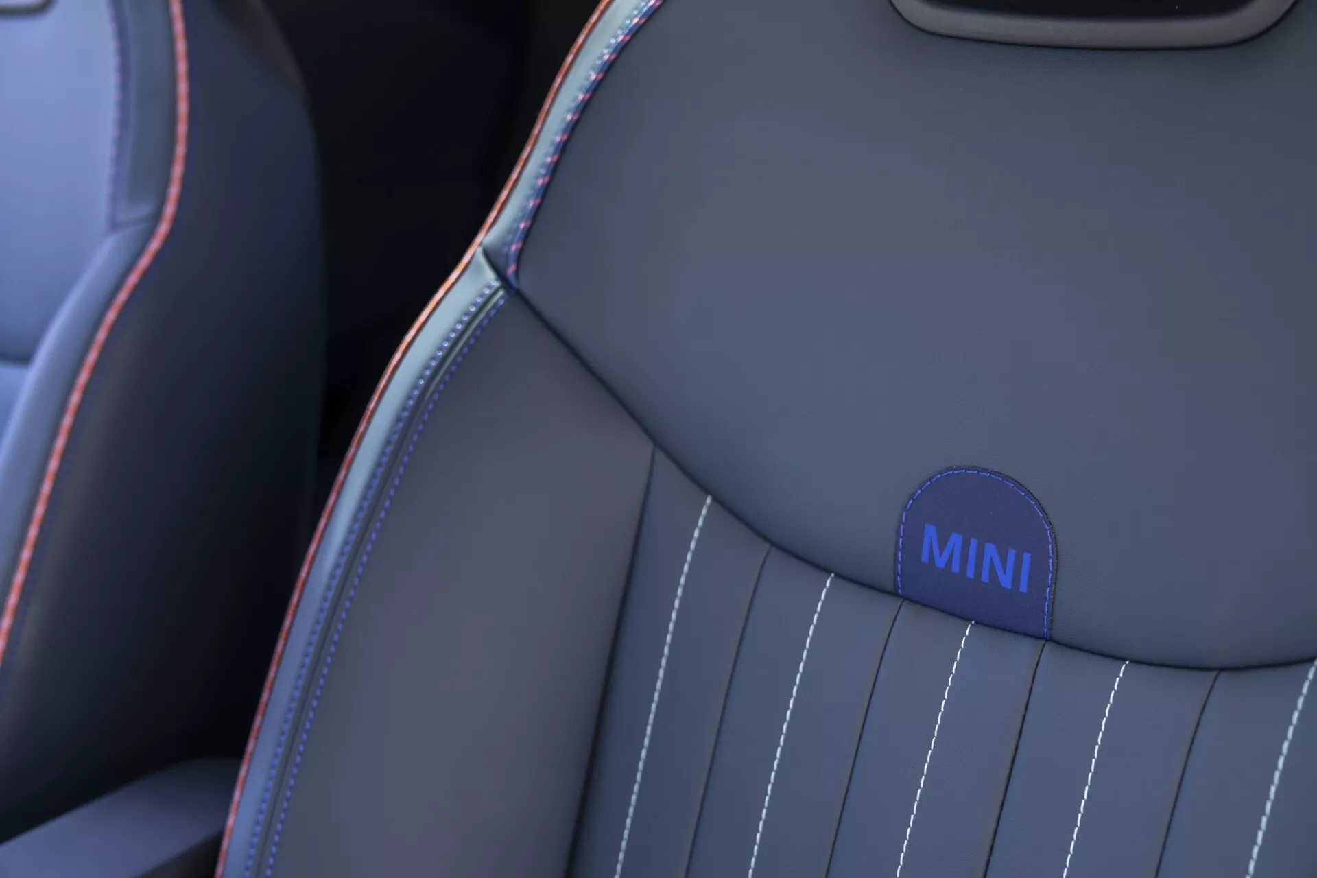 Gros plan sur le siège de la MINI Aceman 2024 mettant en évidence la partie supérieure de l'épaule avec un badge brodé, des coutures contrastées, et un design à rayures verticales en gris et bleu