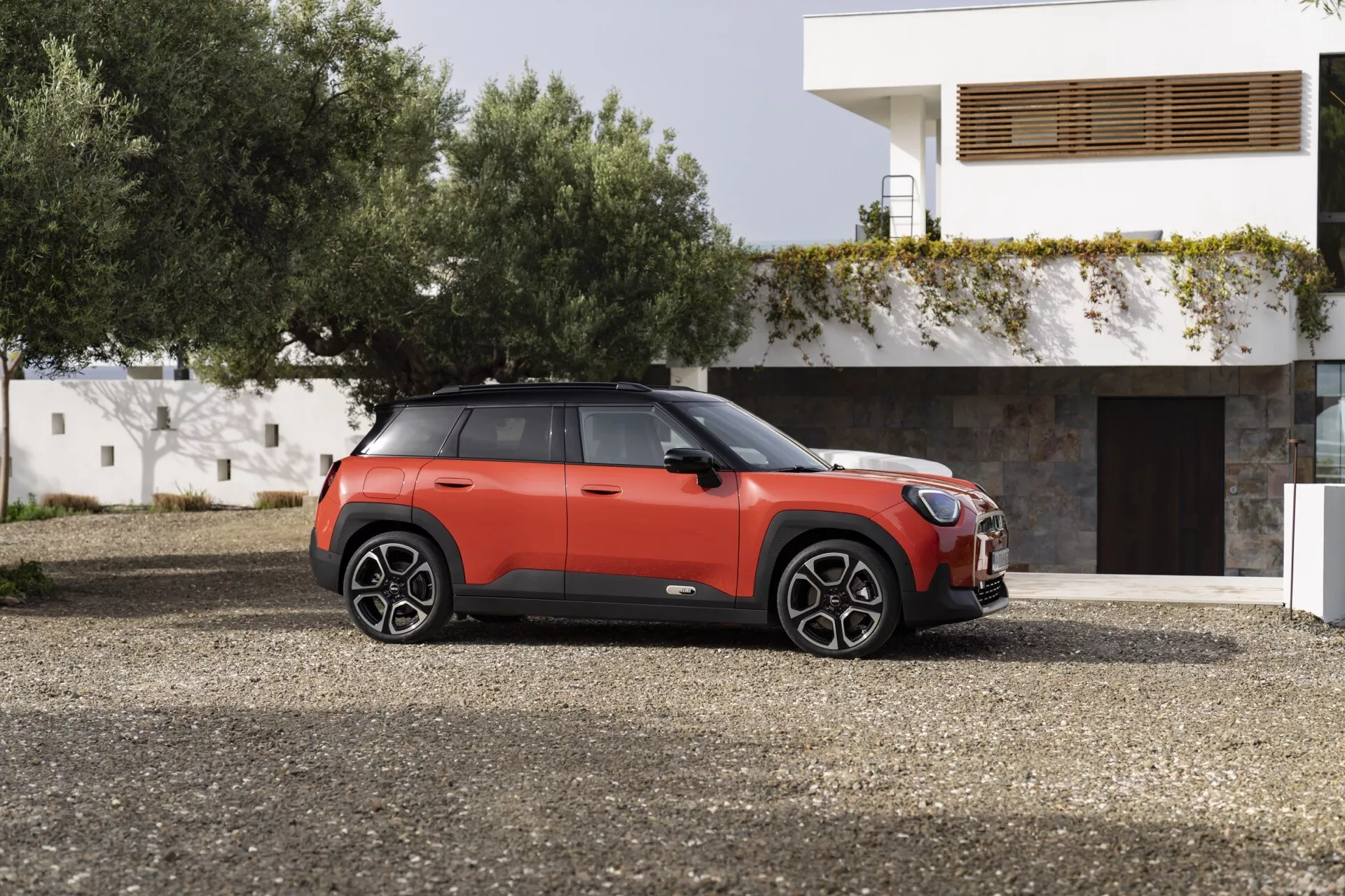 Mini Aceman (J05) 2024 en deux tons rouge et noir présentant un profil latéral sur gravier avec de grandes roues en alliage à multiples rayons, vitres teintées et caractéristiques modernes de SUV