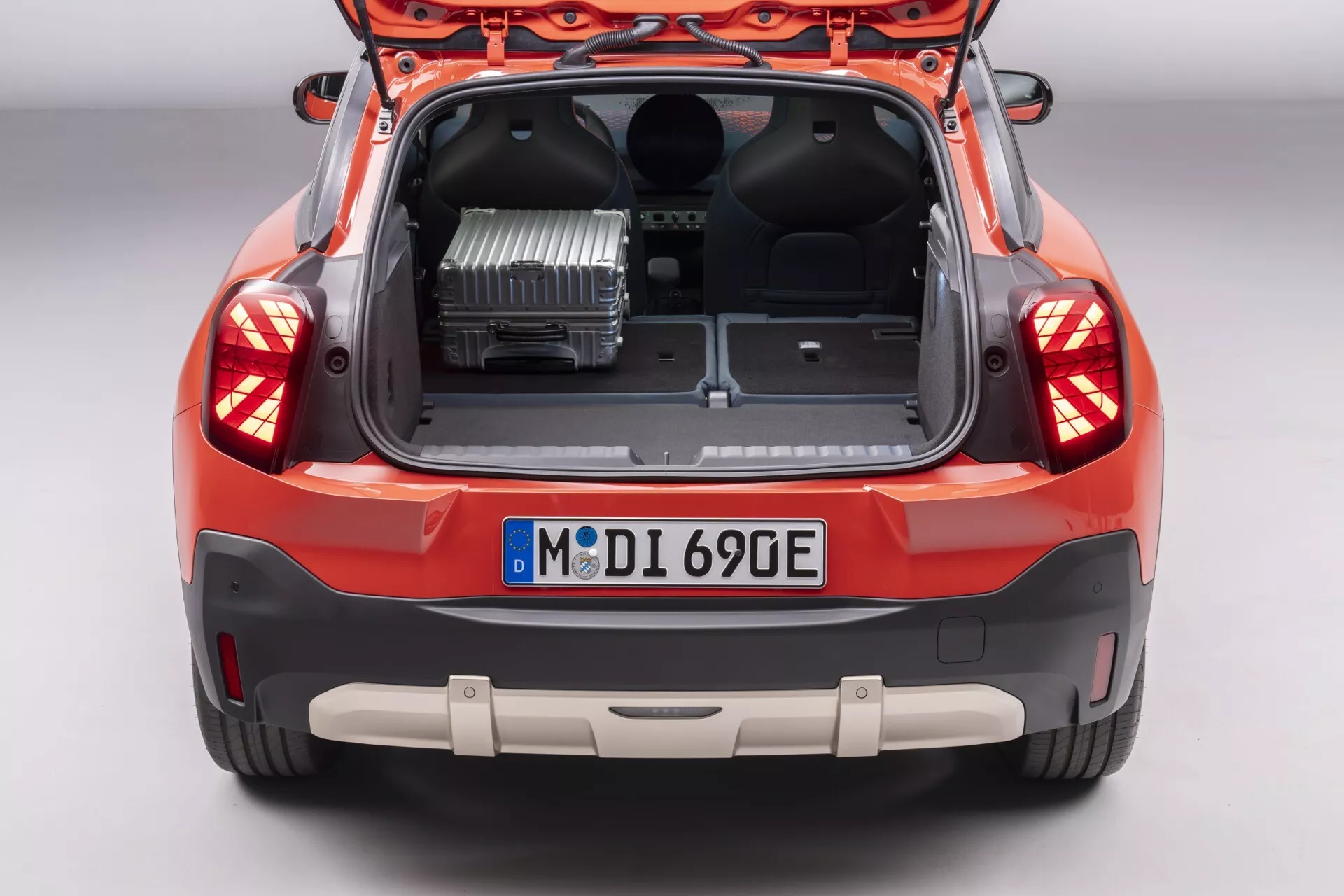 Vue arrière en plongée du Mini Aceman (JO5) 2024 montrant le coffre ouvert avec un onduleur de puissance, un grand espace de chargement, des feux arrière à LED et des capteurs de stationnement sur un fond neutre de studio
