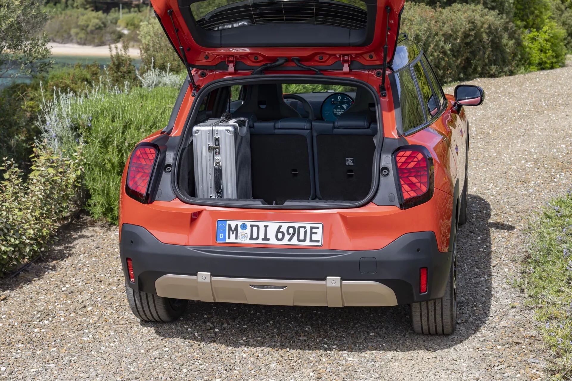 Mini Aceman (J05) 2024 en rouge, présentant le design arrière avec hayon ouvert, valise chargée dans l'espace de coffre plat, indicateurs de modèle électrique, et feux arrière modernes, sur fond naturel