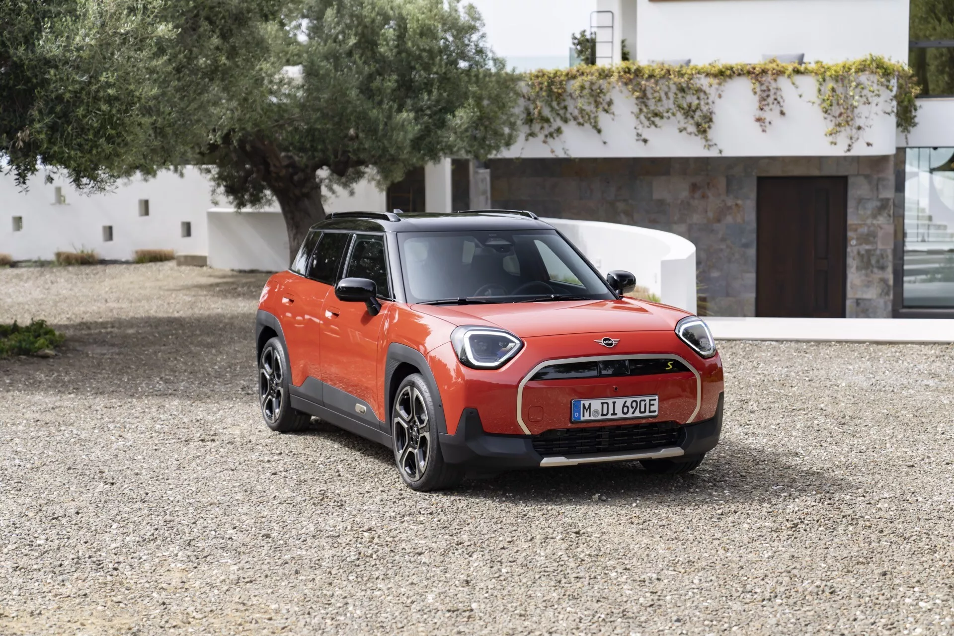 Mini Aceman 2024 (JO5) en orange vif et noir garée à l'extérieur sur du gravier, présentant son design de hatchback compact électrique avec phares LED, grille fermée, roues en alliage à multiples rayons et port de chargement