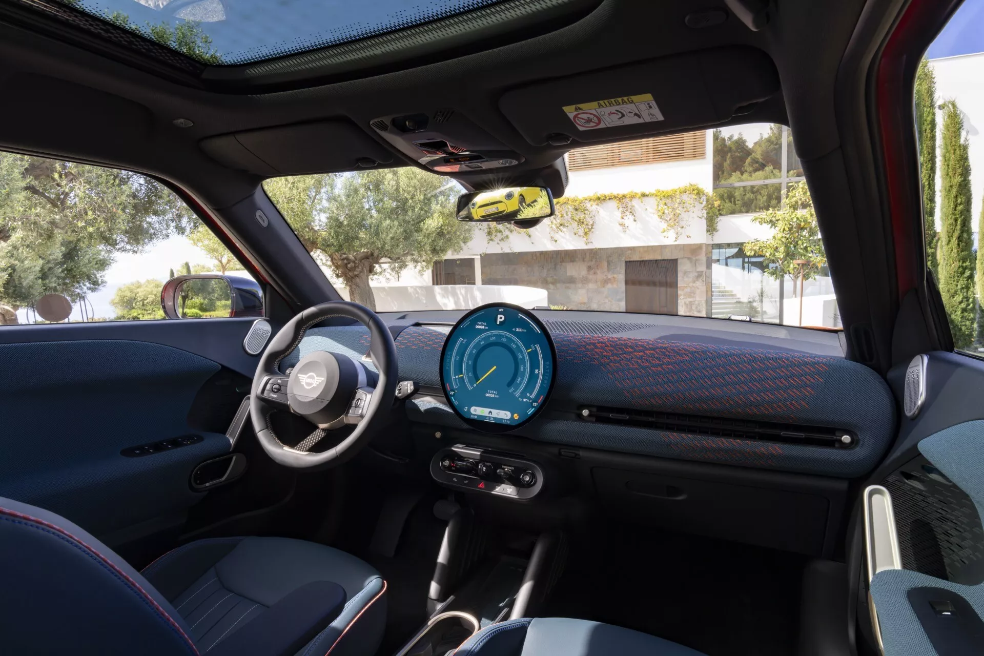 Vue intérieure de la Mini Aceman 2024 (J05) présentant le tableau de bord, le cluster d'instruments numériques, le volant avec boutons multimédias et régulateur de vitesse, les commandes de vitres et rétroviseurs sur la porte du conducteur, matériaux texturés sportifs et toit panoramique au jour