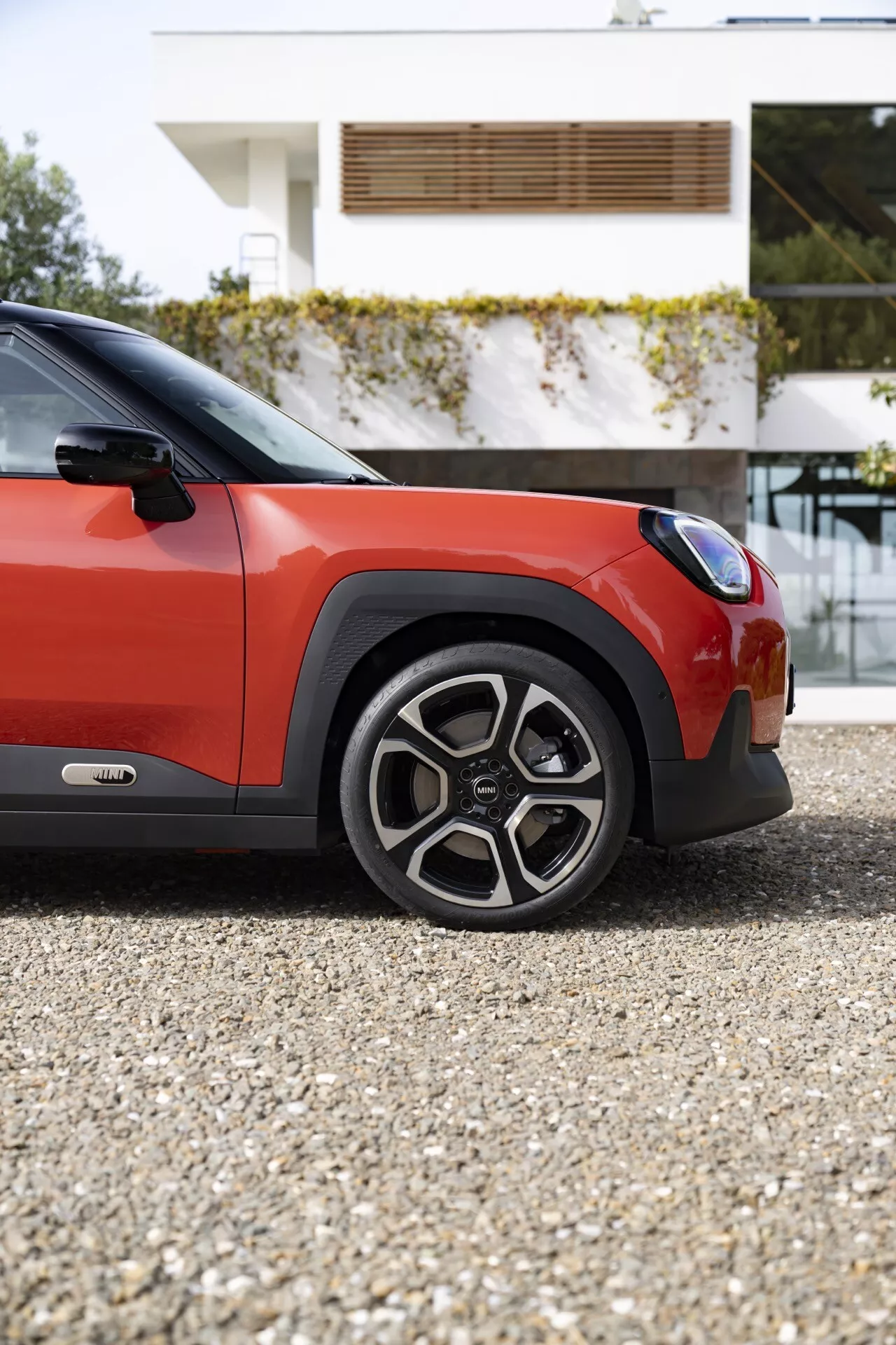 Vue rapprochée du MINI Aceman 2024 (JO5) mettant en avant la roue, l'aile avant et la porte sous un angle bas, soulignant le schéma de couleurs bicolore et les éléments de design robuste et sportif de la voiture.