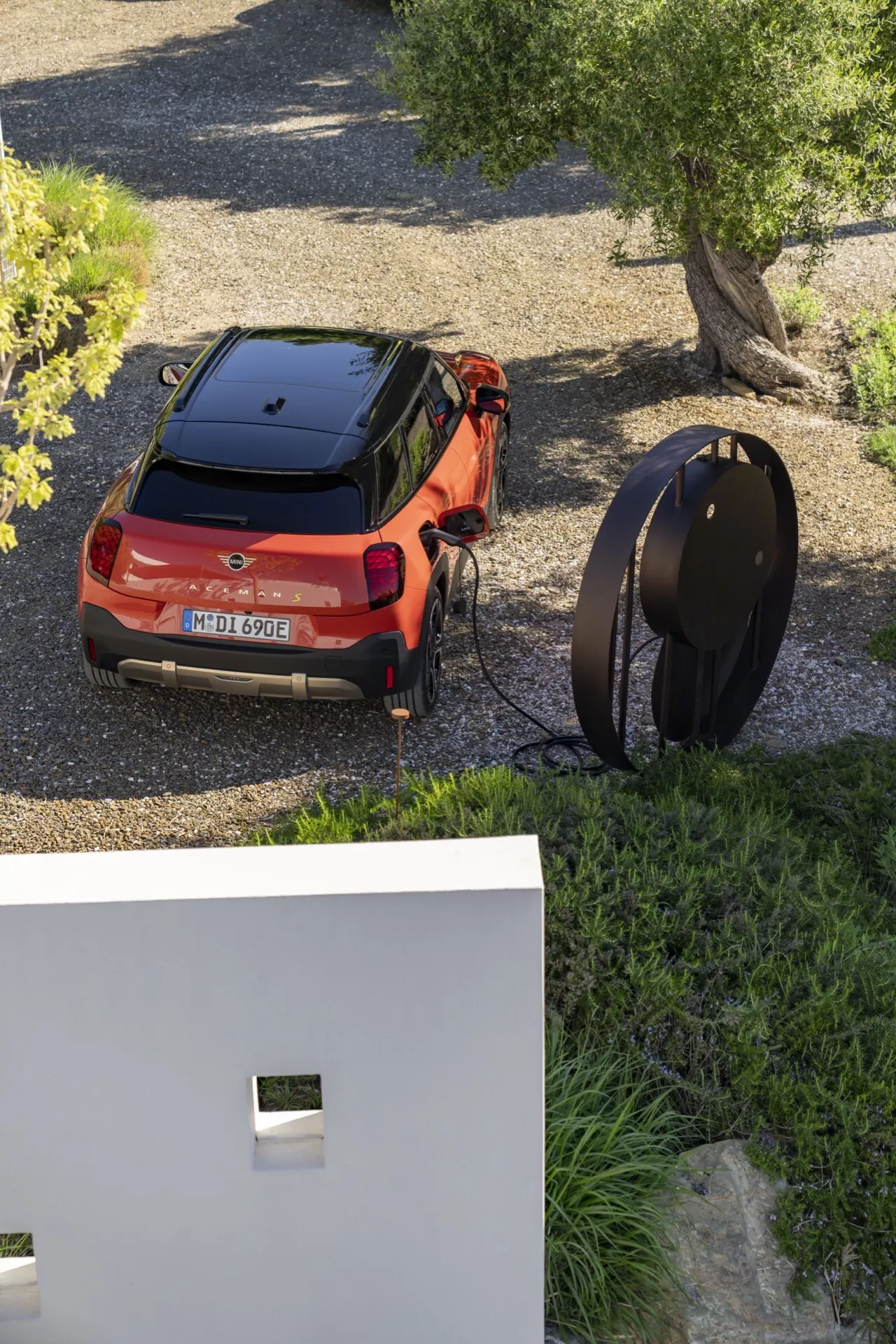 Vue en plongée d'un SUV Mini Aceman (J05) 2024 orange, parqué et en charge, présentant son design contemporain avec un schéma de couleurs bicolore, des feux arrière fins et la capacité de charge électrique, dans un cadre résidentiel moderne