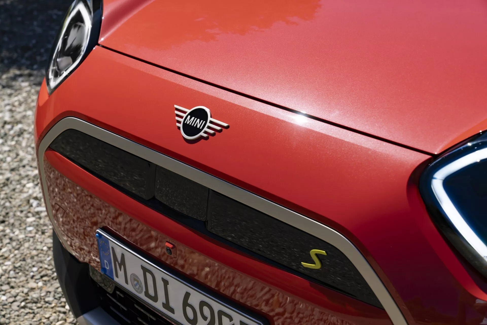 Vue rapprochée d'une Mini Cooper rouge 2024 Aceman (J05) montrant la section avant, incluant le logo Mini, une grille sportive en nid d'abeille avec un badge 'S', un phare LED partiel et des détails dynamiques de conception de la voiture.