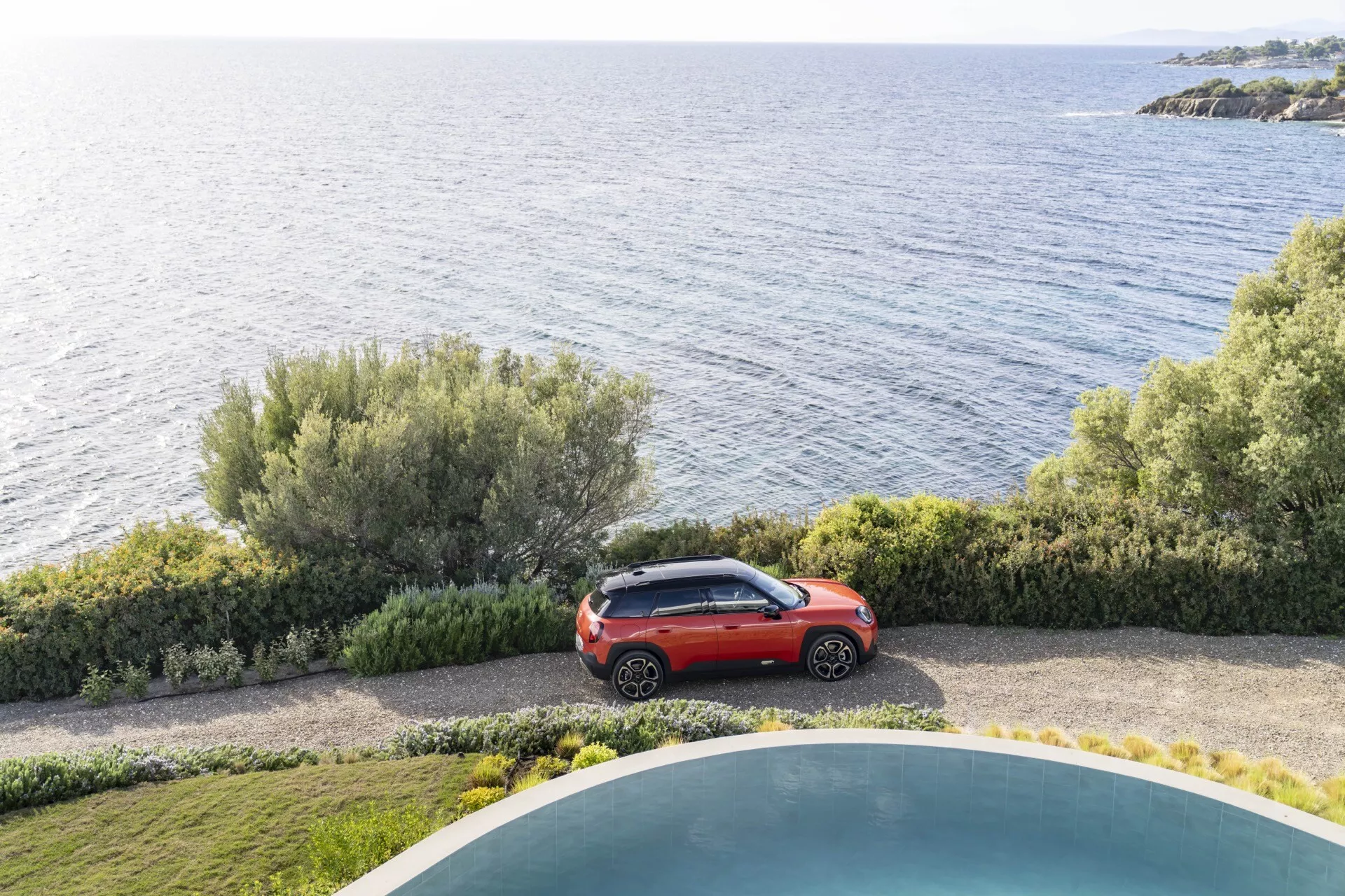 Mini Aceman 2024 (J05) en rouge vif stationné près de la mer à côté d'un jardin bien entretenu et d'une piscine, présentant son design de SUV compact et esthétique moderne sous un angle élevé