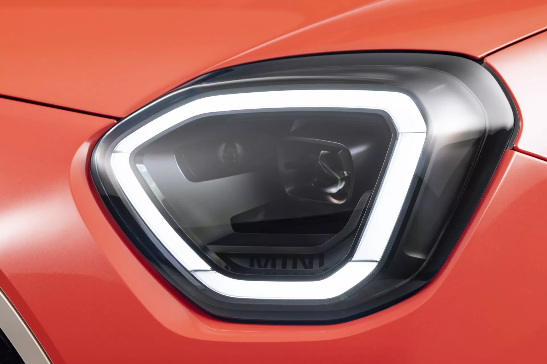 Gros plan sur le phare gauche de la Mini Aceman (J05) 2024 avec technologie LED, lignes angulaires nettes et boîtier onyx-noir contre une carrosserie rouge vif