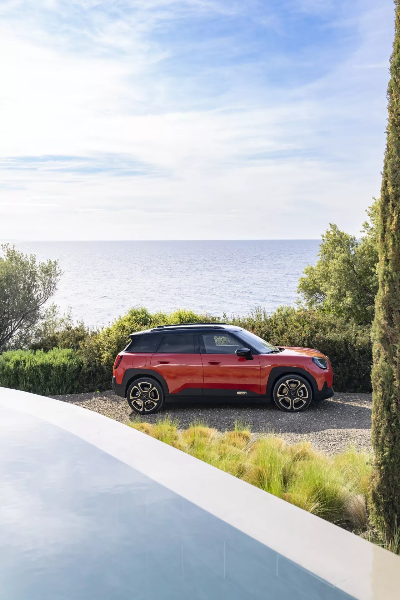 Mini Aceman (J05) 2024 garée sur un chemin de gravier à côté de la mer, présentant sa finition rouge brillante, de grandes roues en alliage et un design moderne de SUV sous un ciel dégagé