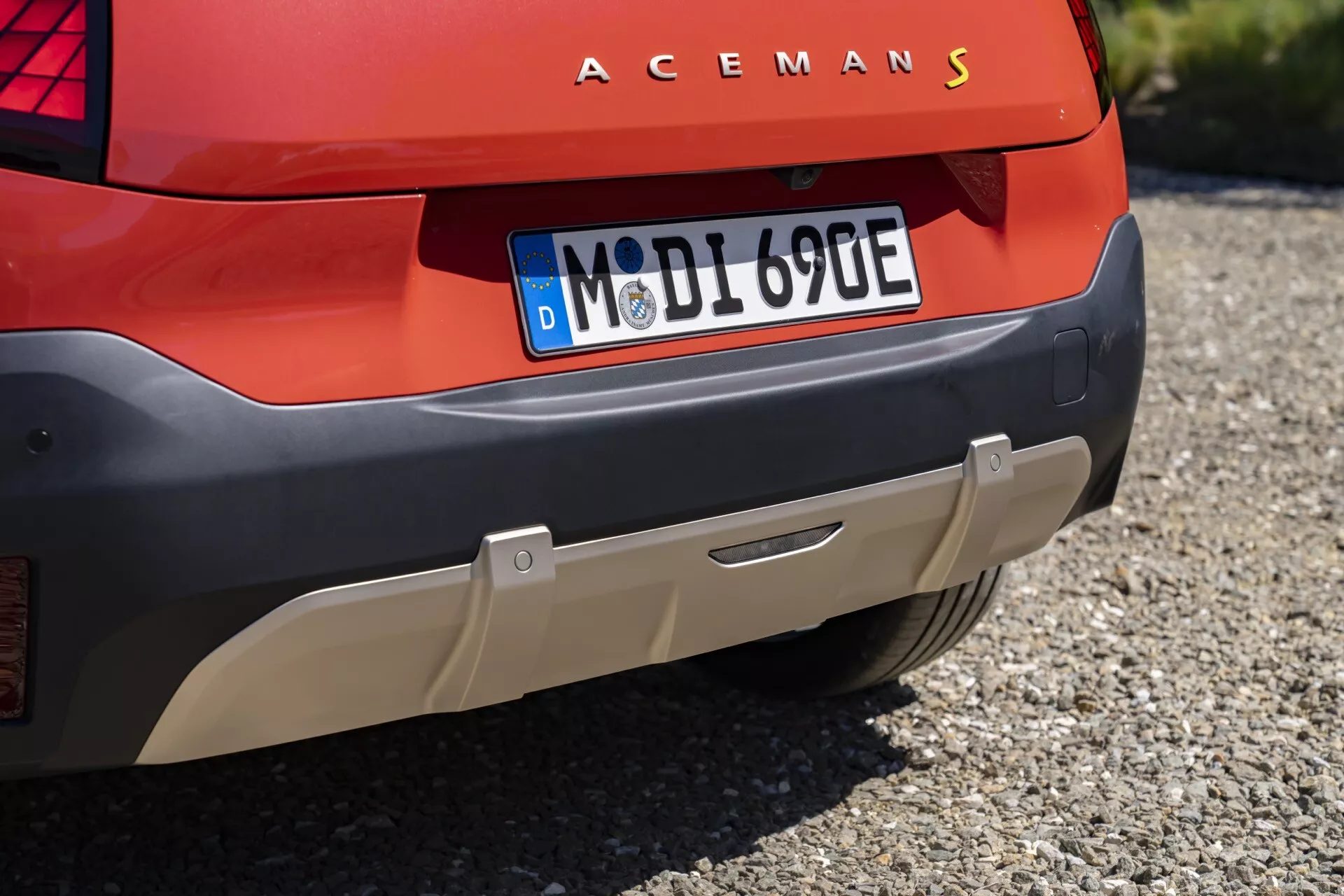 Gros plan sur l'arrière du Mini Aceman 2024 avec l'inscription ACEMANS, design moderne des feux arrière LED, plaque d'immatriculation européenne et capteurs de stationnement sur carrosserie rouge, suggérant un modèle électrique ou hybride.