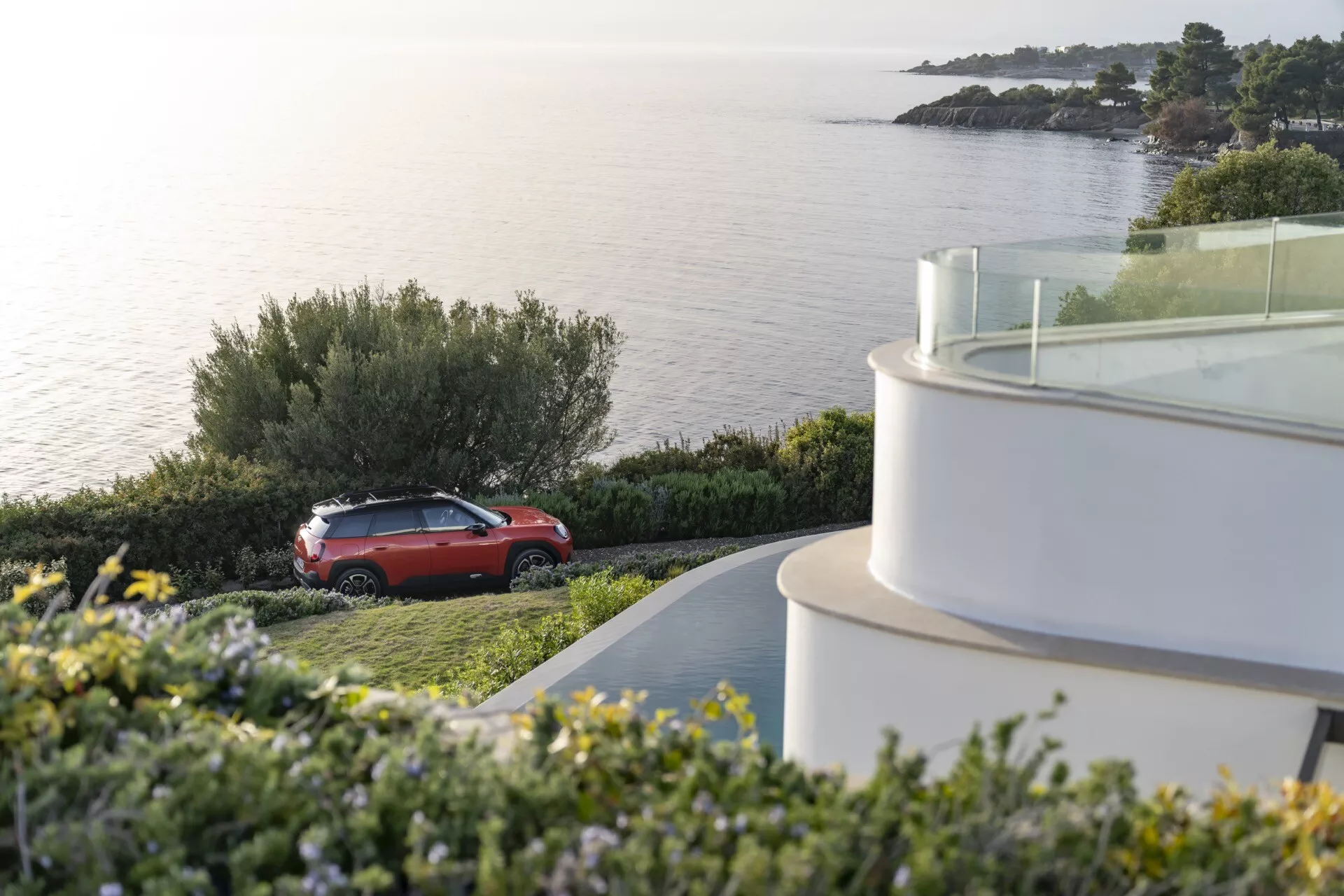 Mini Aceman (J05) de 2024 en rouge garée à l'extérieur dans un cadre côtier, montrant son profil latéral de SUV, les éléments de design et les roues en alliage sur fond de mer calme et de verdure naturelle