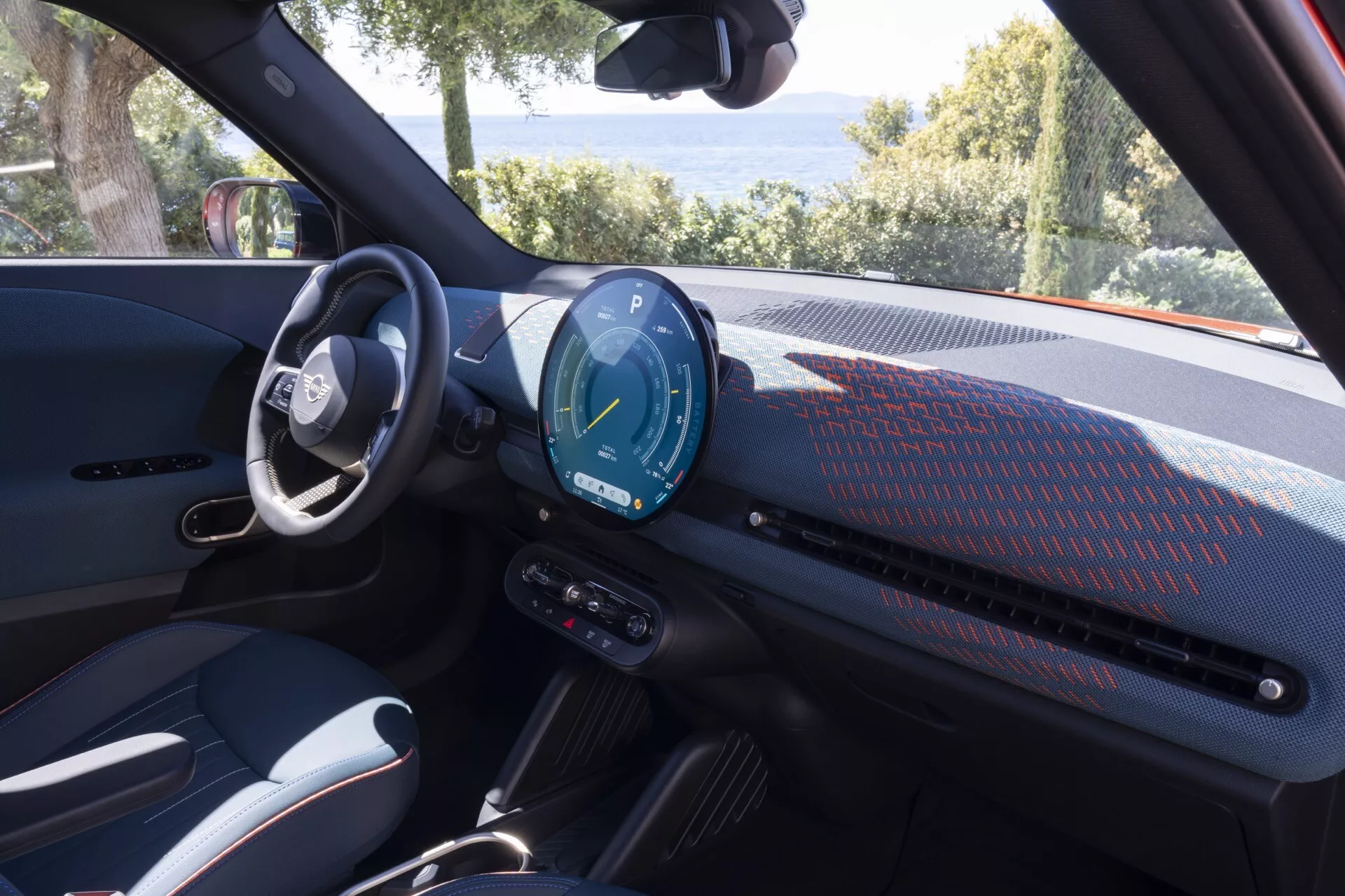 Vue intérieure du Mini Aceman 2024 (JO5) mettant en lumière la zone du conducteur avec un tableau de bord moderne, un cluster d'instruments numériques et des commandes avancées sur le volant, garée dans un cadre naturel