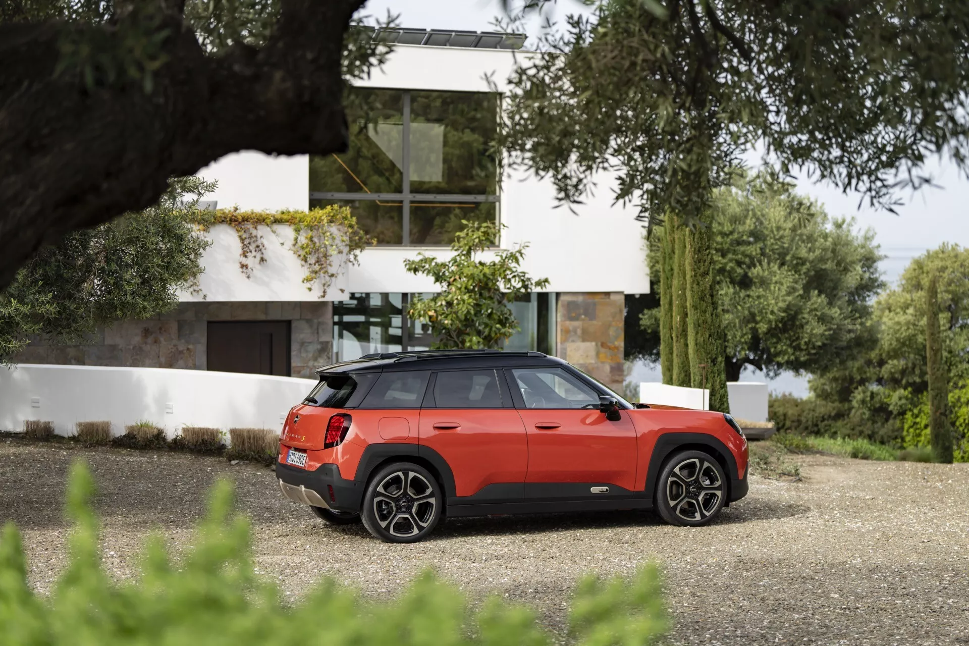 Mini Aceman 2024 (J05) en rouge métallisé garée sur une allée, mettant en avant son design sportif et luxueux avec un toit panoramique, des jantes en alliage, un éclairage arrière LED et des fonctionnalités de sécurité avancées dans un cadre résidentiel contemporain