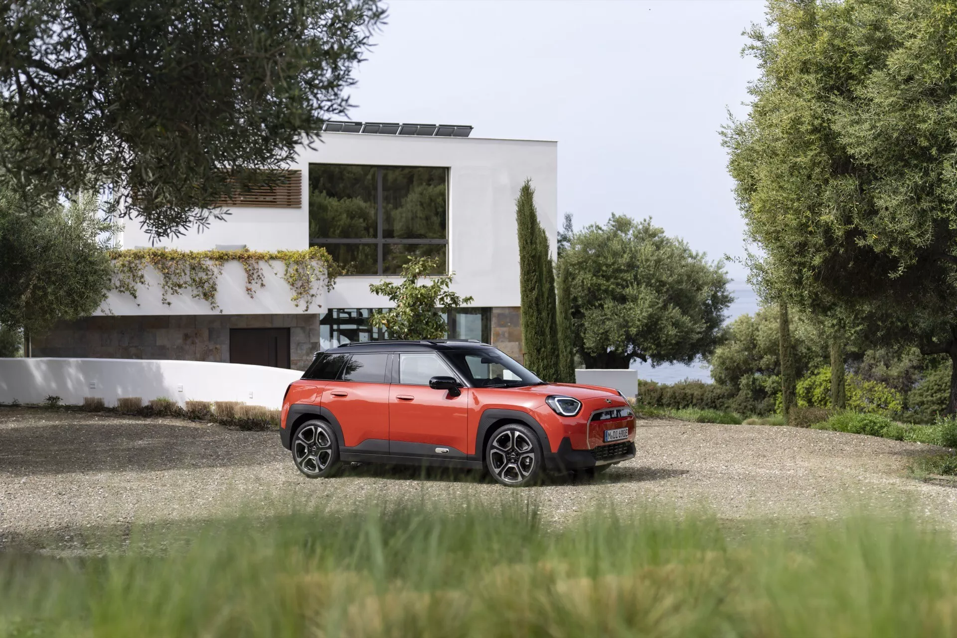 Mini Aceman 2024 (J05) en orange vif avec toit et accents noirs, positionnée sur une allée près d'une maison moderne, montrant la vue latérale et partielle arrière avec des lignes de design élégantes et des roues en alliage.