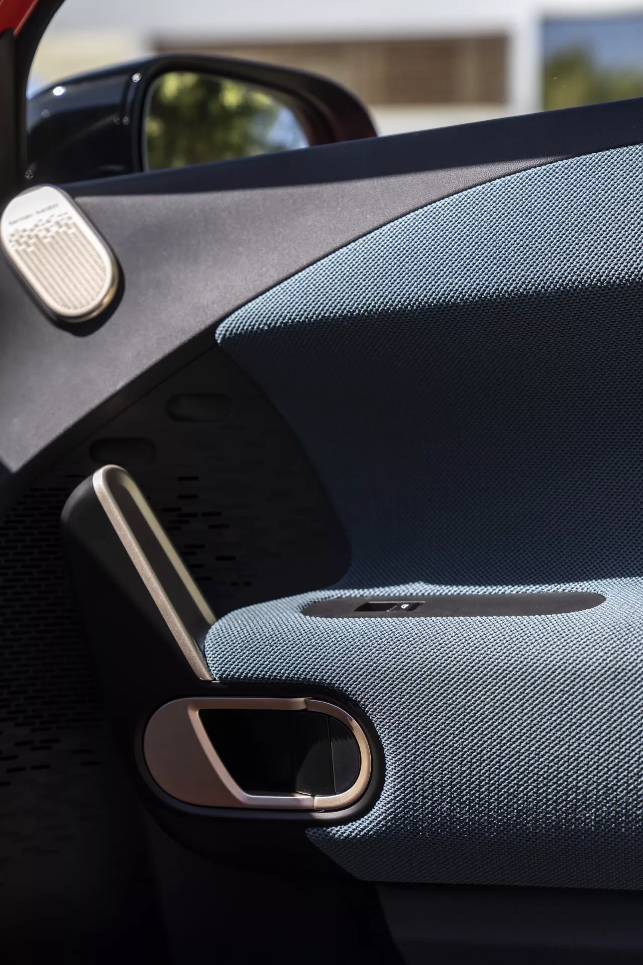 Vue rapprochée de l'intérieur de la porte d'une Mini Aceman (J05) 2024, mettant en avant un accoudoir luxueux, une poignée de porte en métal élégant, une grille de haut-parleur premium intégrée et des matériaux de haute qualité visant à améliorer le confort de l'utilisateur et l'esthétique du véhicule