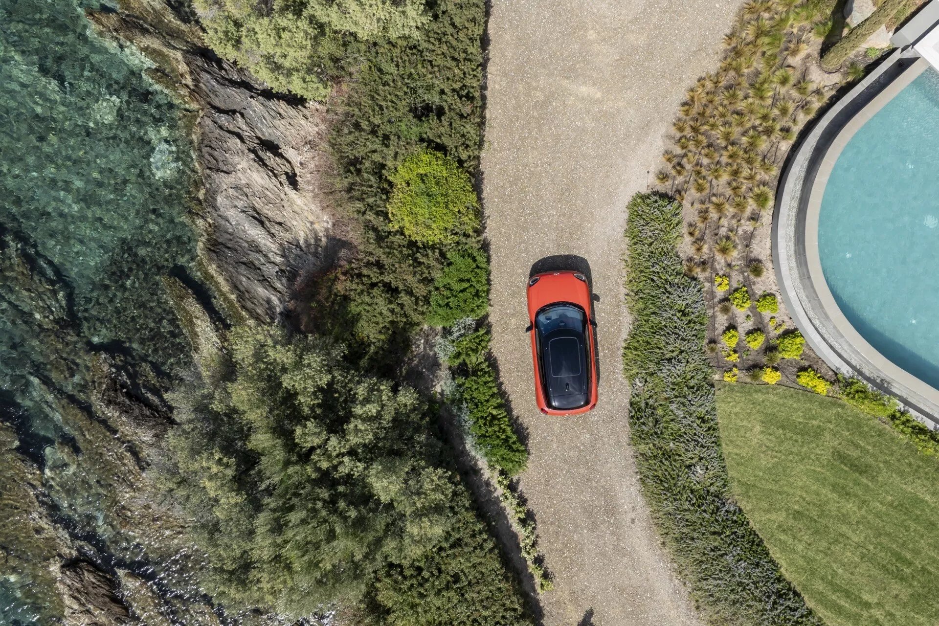 Vue aérienne de la Mini Aceman 2024 (J05) exposant son toit, capot, coffre et une partie de son profil latéral, stationnée près d'une falaise et d'un plan d'eau, entourée d'une végétation luxuriante, mettant en avant la caractéristique du toit ouvrant de la voiture