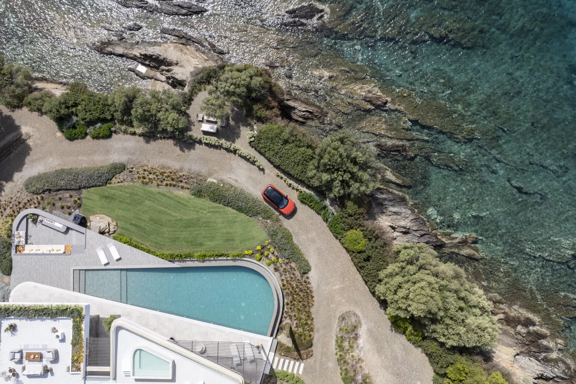 Vue aérienne d'une Mini Aceman 2024 (J05) rouge garée sur une allée privée près de la côte, entourée de paysages naturels et d'équipements de luxe