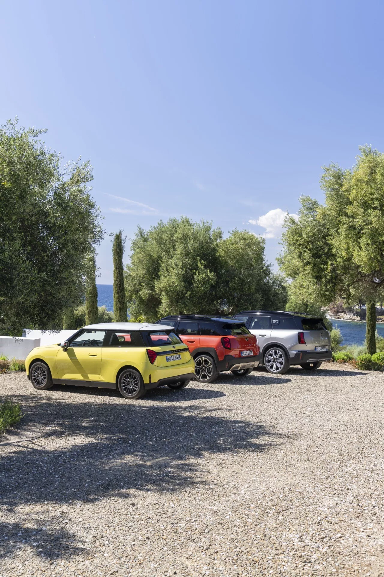 Mini Aceman (J05) 2024 en jaune vif, orange et gris, garée sur une surface de gravier avec un arrière-plan naturel composé d'arbres, d'eau et du ciel, montrant un design moderne avec des lignes nettes, des feux arrière LED et une gamme de taille de compacte à SUV