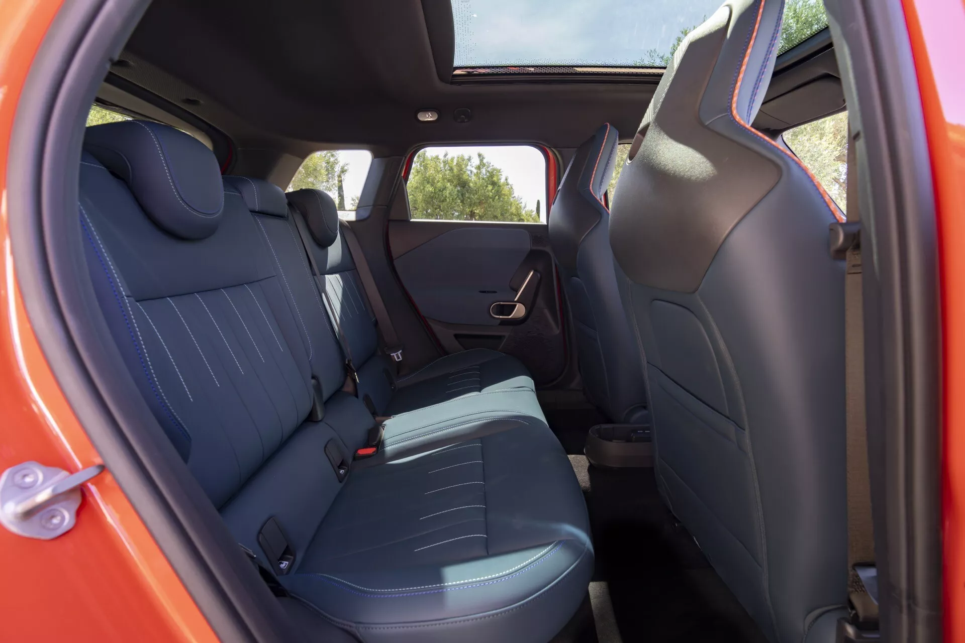 Vue intérieure du MINI Aceman (J05) 2024 montrant les sièges arrière à travers la porte passager ouverte d'un angle extérieur bas à moyen, avec une garniture sombre soulignée de bleu, des appuis-tête intégrés et des éléments de design moderne