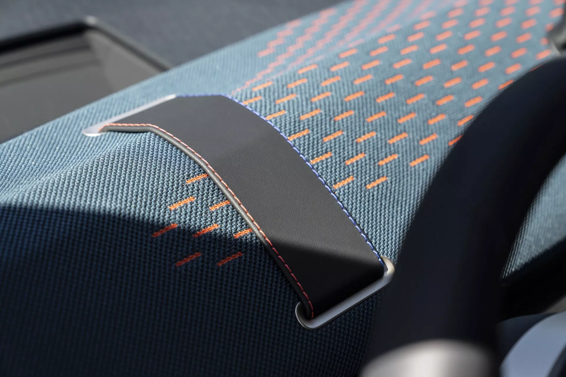 Image en gros plan de l'intérieur d'une Mini Aceman (J05) 2024 mettant en évidence le clip de ceinture de sécurité, montrant le tissu du siège avec un motif bleu et orange avec des coutures orange détaillées et la boucle de ceinture de sécurité métallique avec finition chromée et des points de suture en marron rougeâtre.