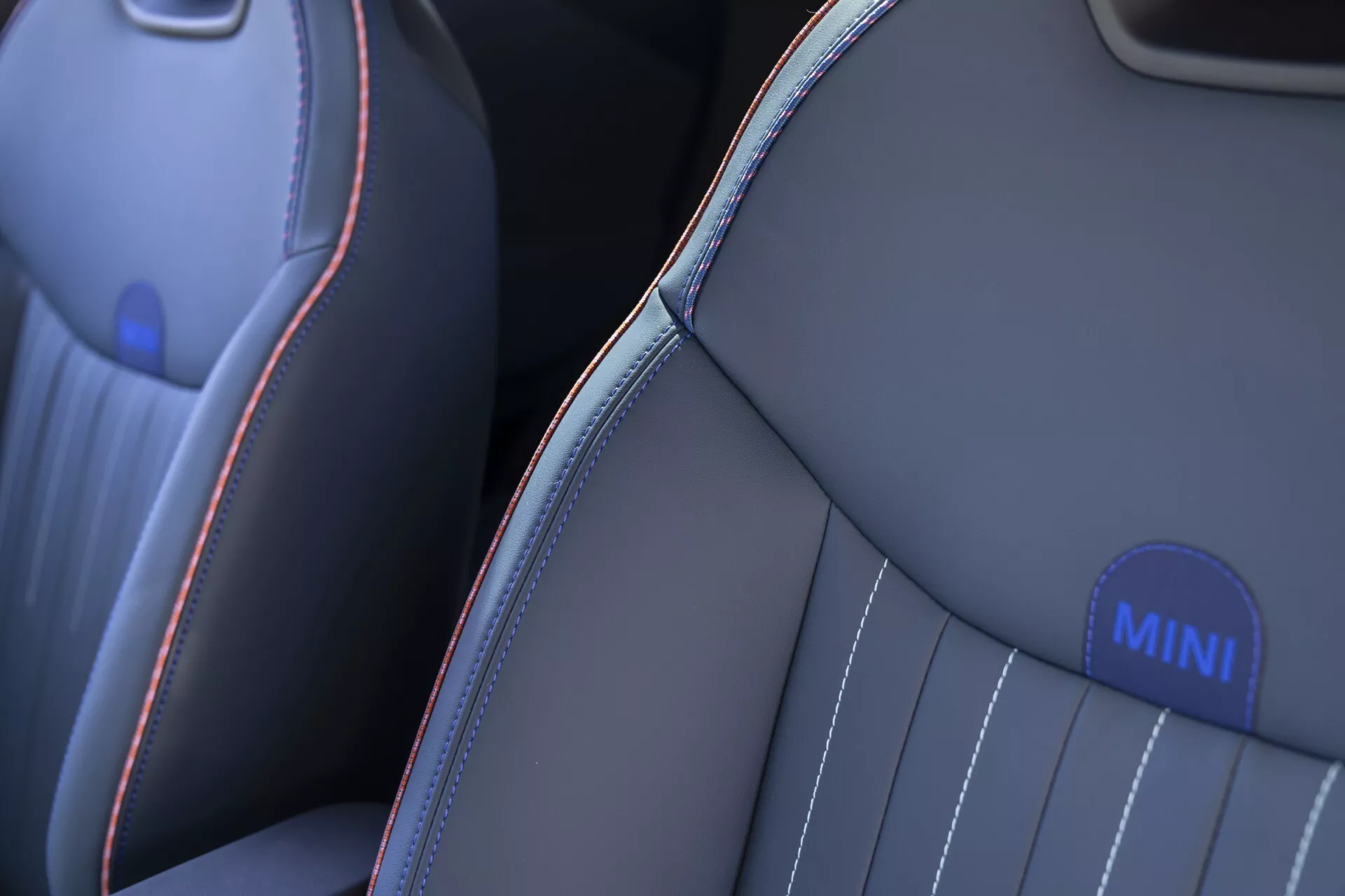 Vue rapprochée du siège avant du MINI Aceman 2024 (J05) montrant une garniture haut de gamme en gris foncé ou noir avec des coutures contrastées rouge et bleu clair, un capitonnage vertical pour le confort et un emblème MINI sur le renfort latéral