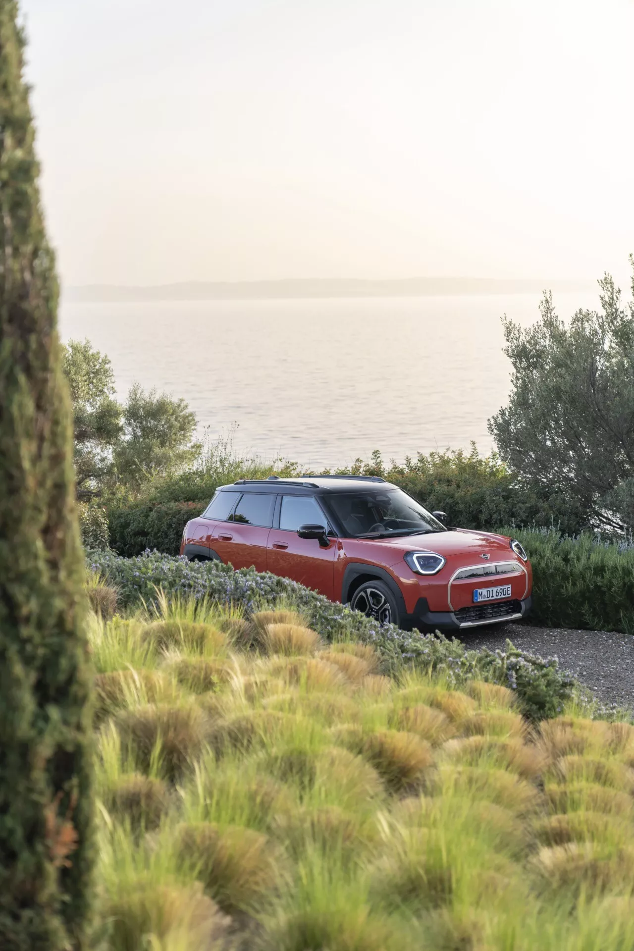 Mini Aceman 2024 (J05) garée en extérieur dans un cadre naturel en journée, présentant une carrosserie rouge ou orange avec toit contrastant, roues en alliage et vue avant trois quarts