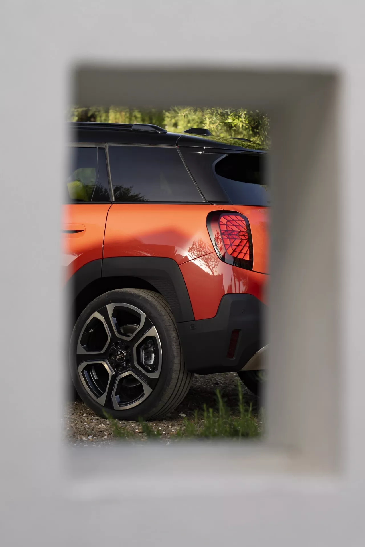 Vue partielle d'une Mini Aceman (J05) 2024 en orange vif, mettant en évidence le quart arrière avec un feu arrière LED circulaire et une roue en alliage sportif à multiples branches