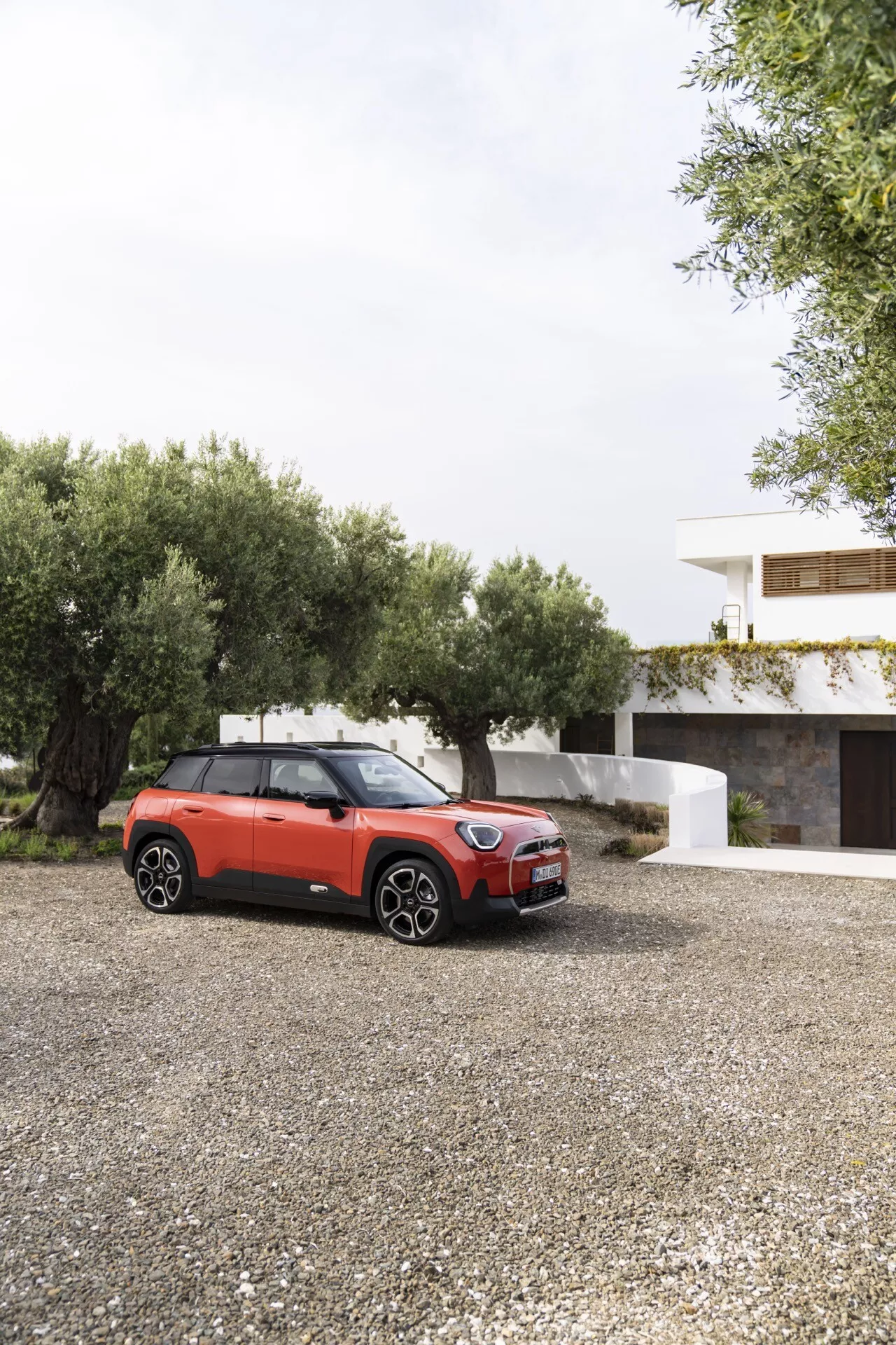 Mini Aceman 2024 (J05) vue de trois quarts avant mettant en évidence sa grille avant élégante, phares LED et profil latéral partiel avec porte et fenêtres côté conducteur sur une surface en gravier, présentant des éléments de design urbain moderne et des fonctionnalités technologiques avancées potentielles comme des roues en alliage et un toit solaire panoramique sur fond résidentiel.