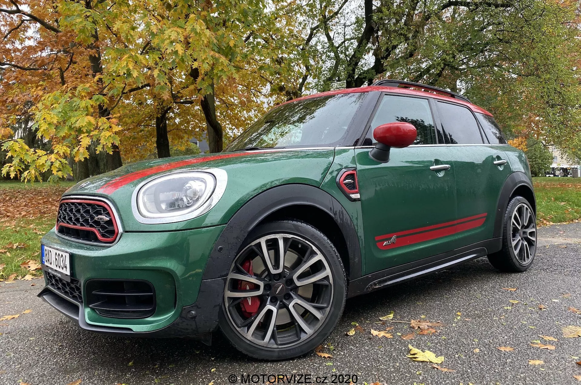 Vue en angle faible à trois quarts avant d'une Mini Countryman John Cooper Works 2020, présentant son extérieur vert foncé avec des accents rouges, des roues sportives à multiples rayons, une grille entourée de chrome, de grandes entrées d'air, des phares à LED et des étriers de frein rouges.