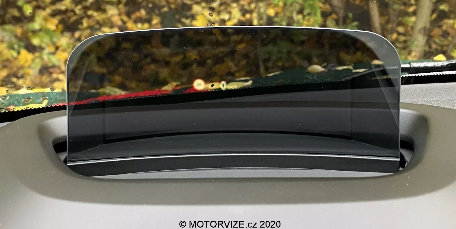 Image mettant en avant l'affichage tête haute (HUD) de la Mini Countryman 2020, projeté sur un écran transparent au-dessus du tableau de bord depuis la perspective du conducteur. Le panneau HUD, clair et semblable à du verre, est parfaitement intégré au design intérieur, arrondi et légèrement incliné pour une visibilité optimale. L'arrière-plan à l'extérieur du pare-brise est flou, soulignant l'importance du HUD à présenter des informations de conduite essentielles.