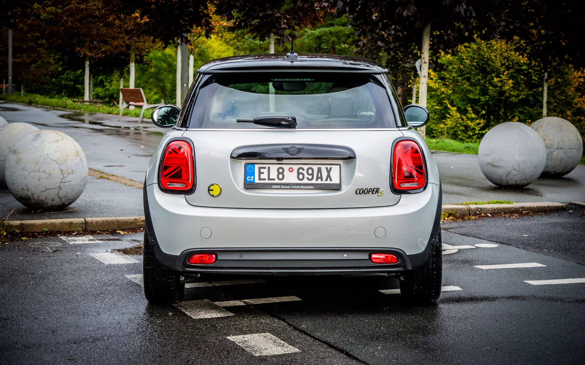 Vue arrière de MINI Électrique 3 Portes 2021 mettant en évidence des feux arrière distinctifs, couvercle du coffre marqué COOPER, pare-brise arrière clair avec essuie-glace, spoiler aérodynamique, emblème et badges du fabricant, pare-chocs arrière avec capteurs de stationnement, et vue partielle des roues arrière dans un parking