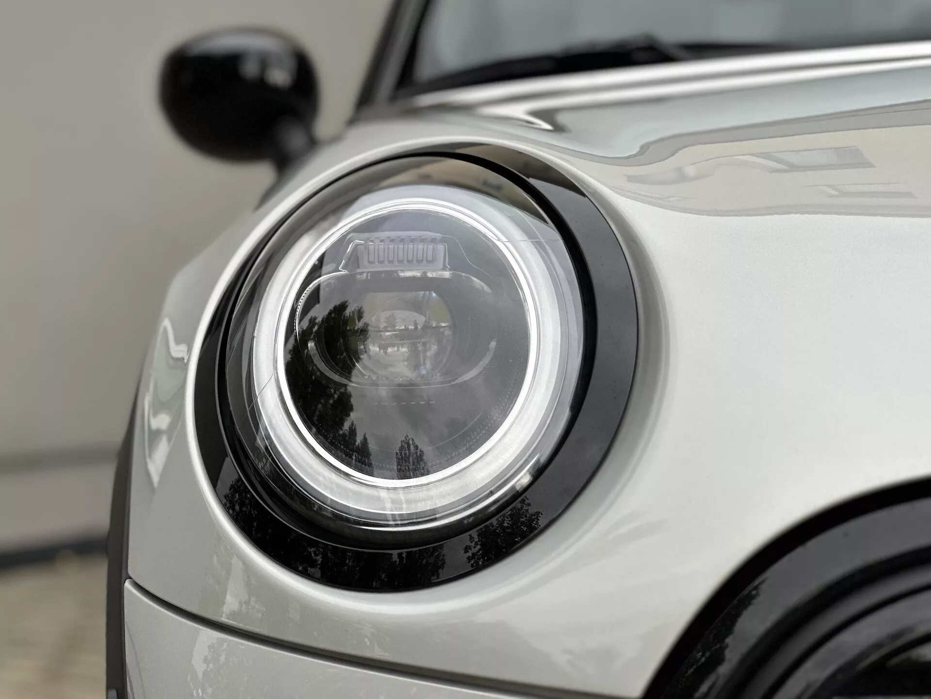 Vue rapprochée du phare d'un modèle Mini Electric 2021 3 portes présentant une technologie LED avancée et une esthétique de conception avec une partie avant partielle et une finition argentée brillante de la voiture visible