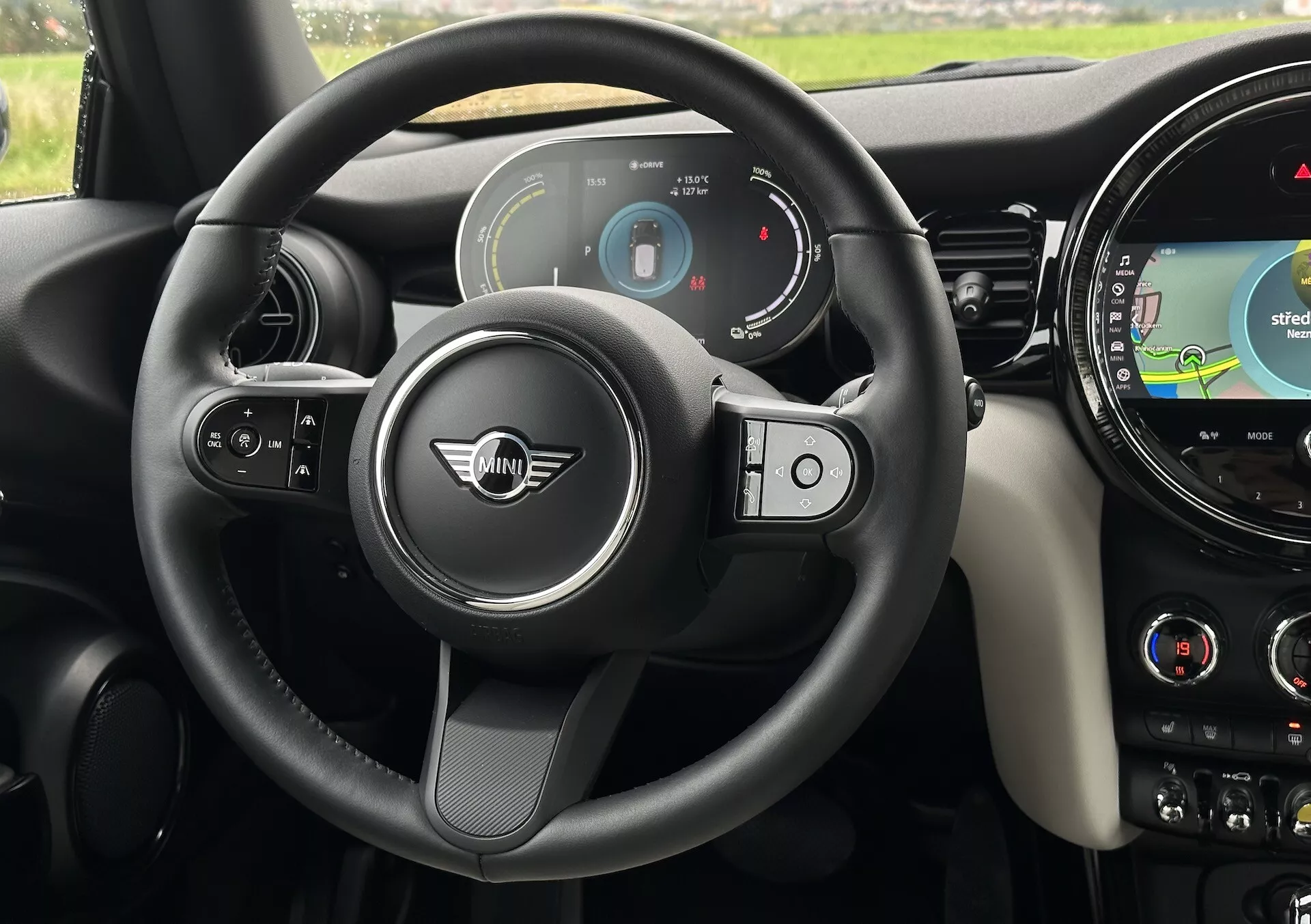 Vue intérieure de la MINI Électrique 3 Portes 2021 montrant le cockpit du point de vue du conducteur, mettant en avant le volant moderne à trois branches avec des boutons multifonctions, le tableau de bord numérique et le système d'infodivertissement avec navigation GPS sur le tableau de bord.