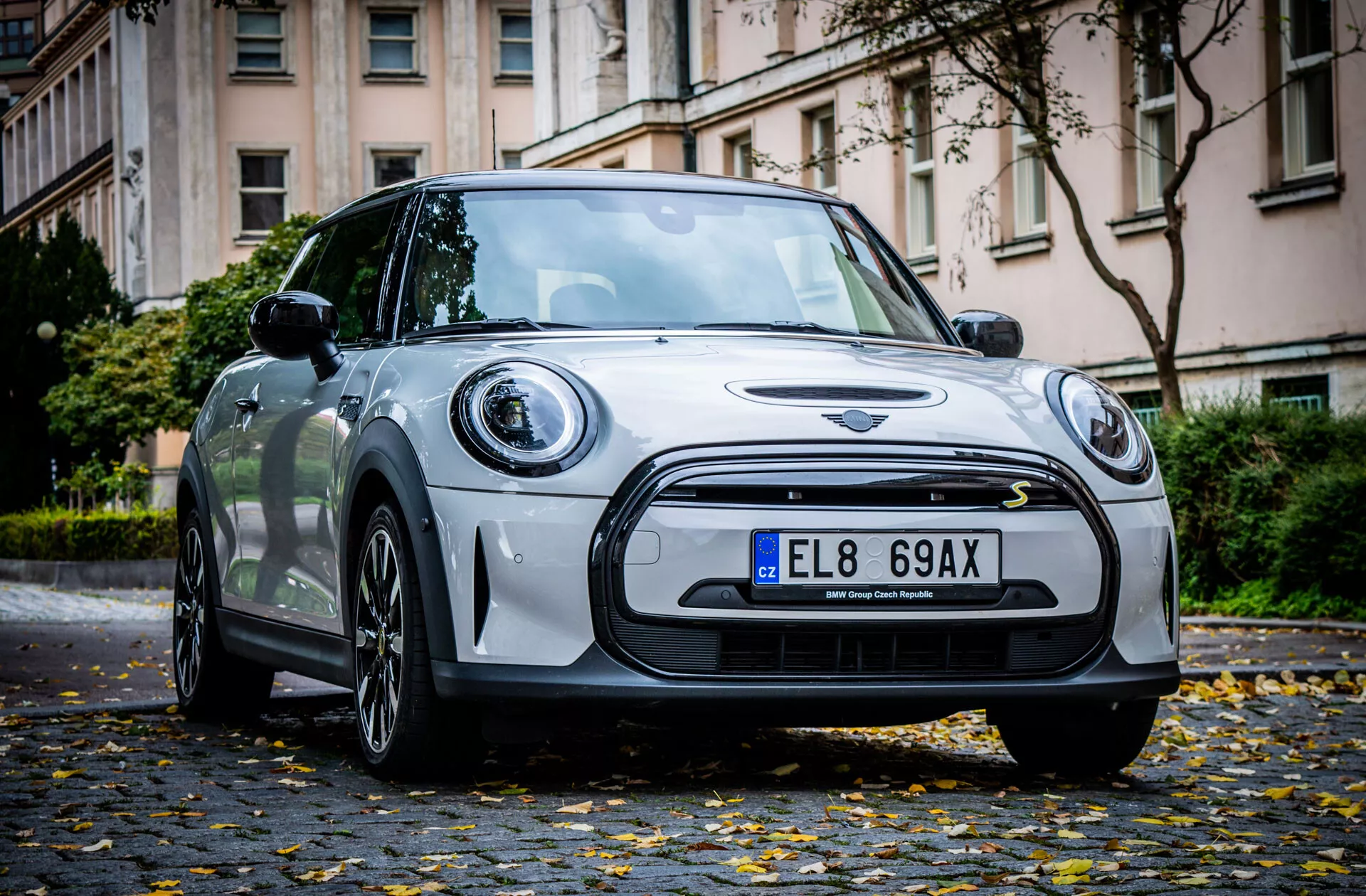Vue d'angle avant d'une hatchback Mini Électrique 3 portes 2021 montrant des phares LED, grille, emblème et jantes en alliage dans une rue urbaine en automne