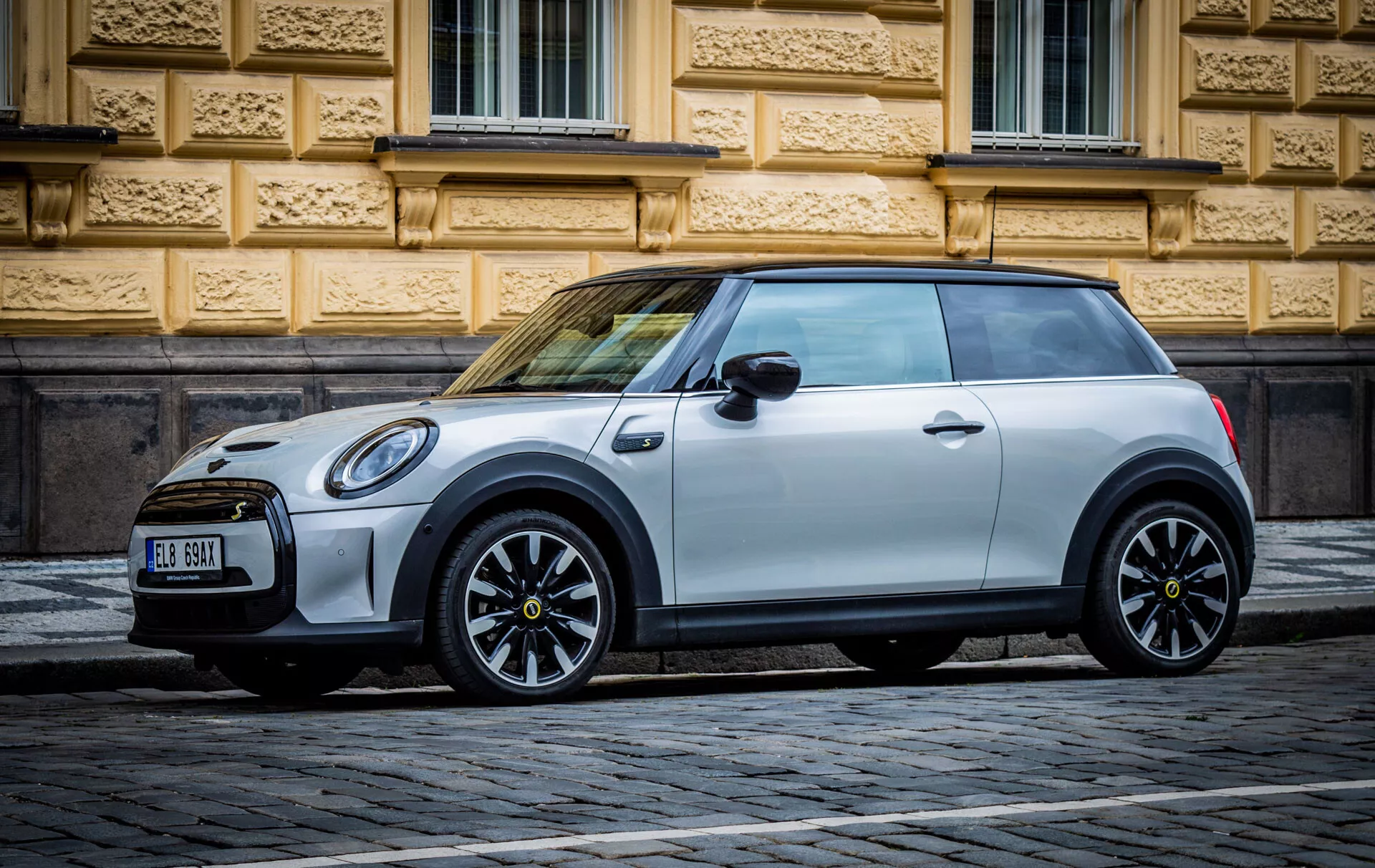 Mini Cooper électrique 3 portes de 2021 garée sur une rue pavée devant un bâtiment historique aux détails architecturaux ornés, mettant en avant son design moderne et ses caractéristiques écologiques