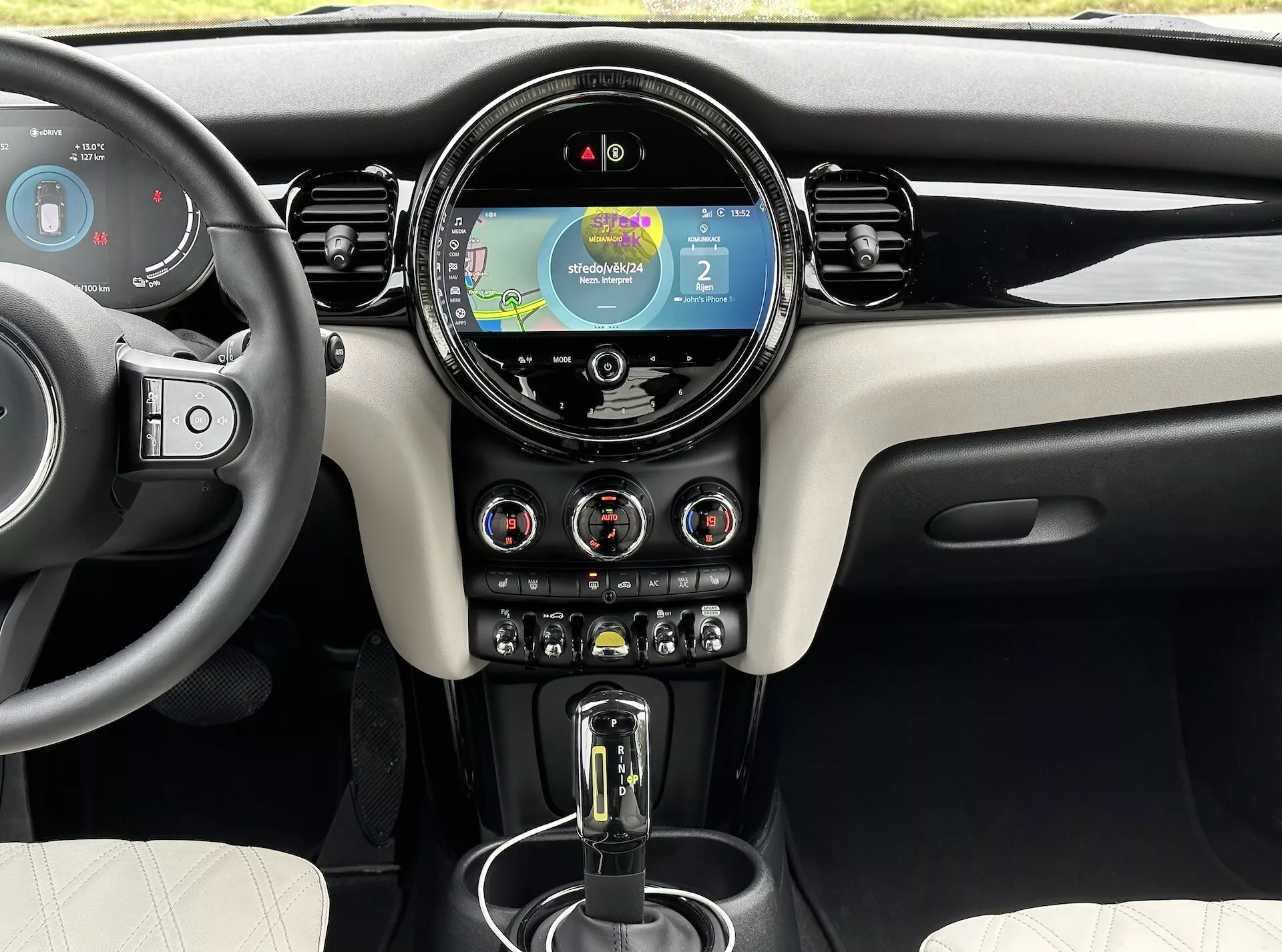 Intérieur du Mini Electric 3-Door 2021 présentant le tableau de bord avant, l'affichage numérique avec navigation, le système d'infodivertissement tactile circulaire central, les interrupteurs de contrôle climatique et le levier de vitesse automatique