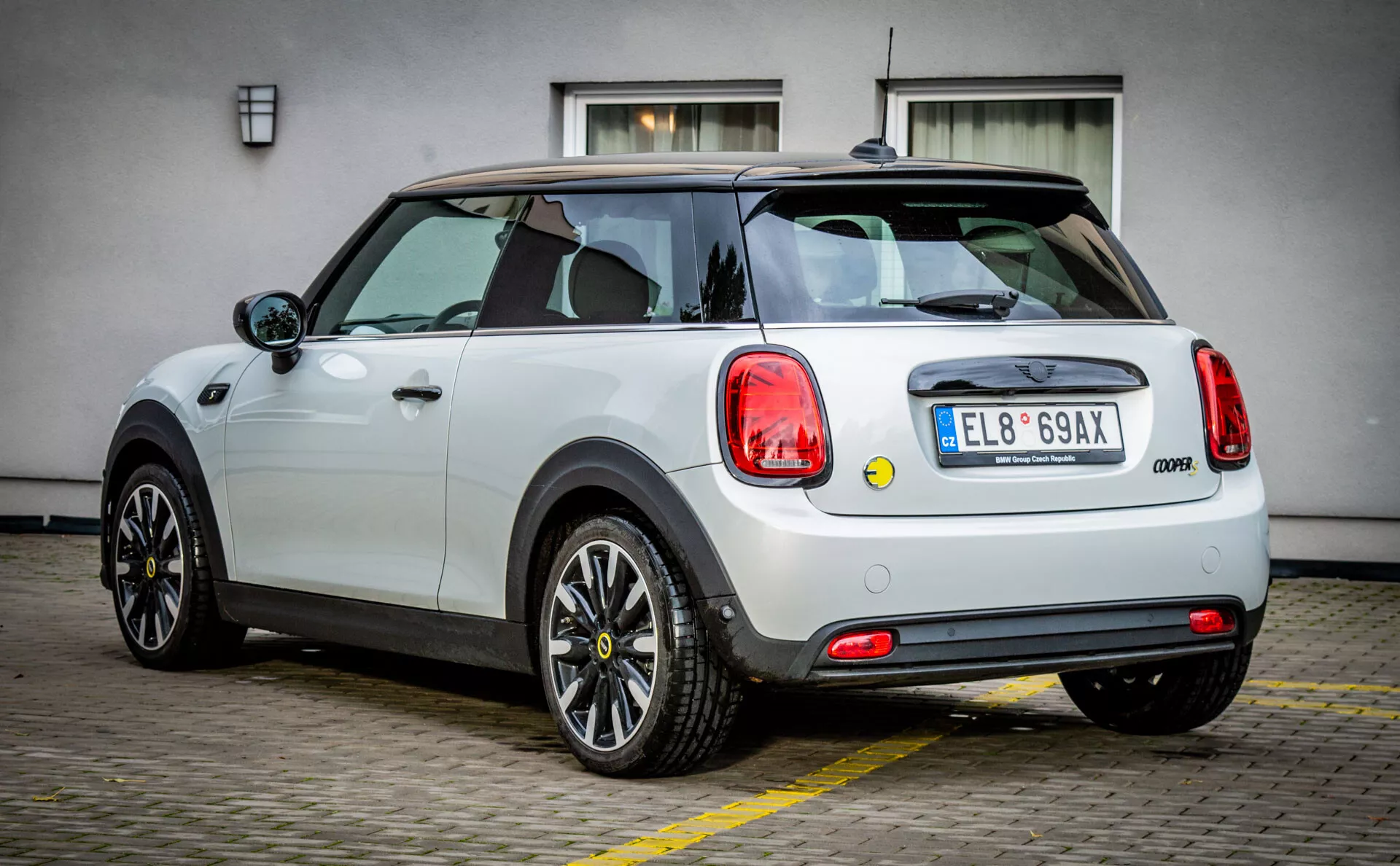 Mini Cooper moderne 2021 électrique 3 portes en blanc avec toit noir, jantes en alliage multi-rayons, fenêtres sans cadre et capteurs de stationnement avancés depuis un angle arrière de trois quarts mettant en avant son design et ses caractéristiques.