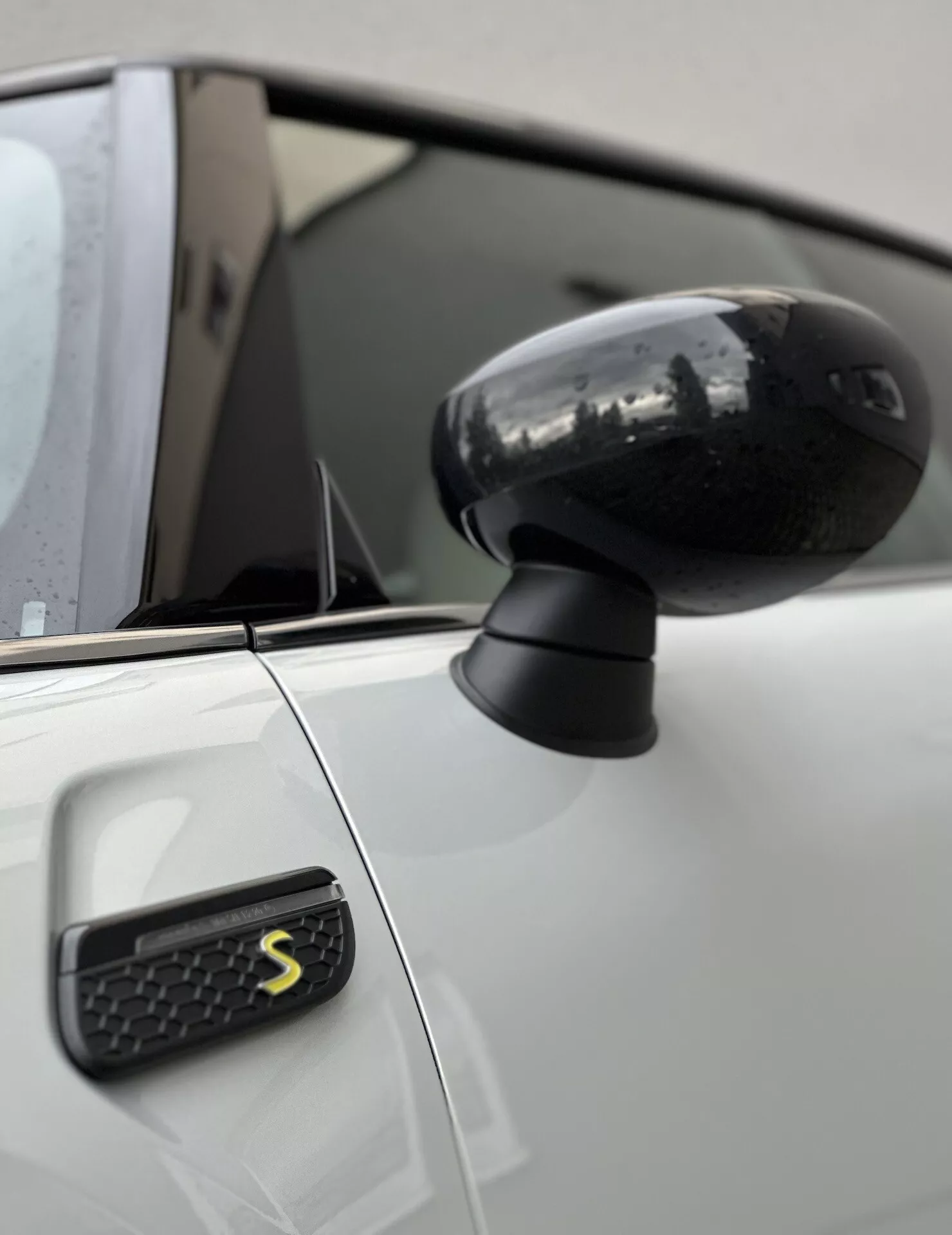 Vue rapprochée du rétroviseur latéral et de l'aile avant de la Mini Electric 3-Door avec un design noir élégant et un emblème stylisé 'S', mettant en valeur l'esthétique moderne du véhicule et la technologie.