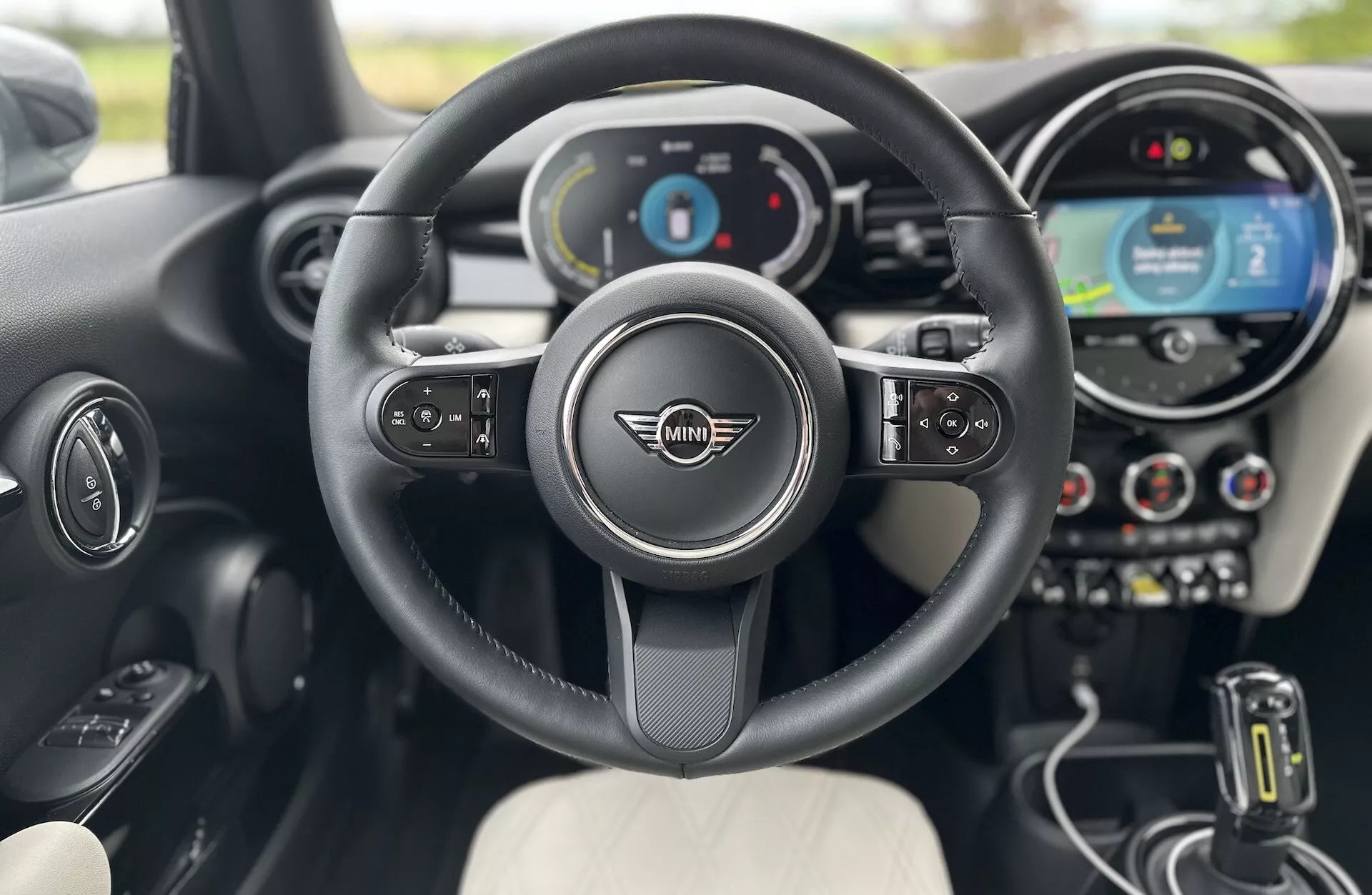 Vue intérieure de la Mini Électrique 3 Portes 2021 du point de vue du conducteur, mettant en vedette le volant multifonction avec l'emblème Mini Cooper, cluster d'instruments numérique, système d'infodivertissement à écran tactile central, sélecteur de vitesse automatique et sièges élégants bicolores.